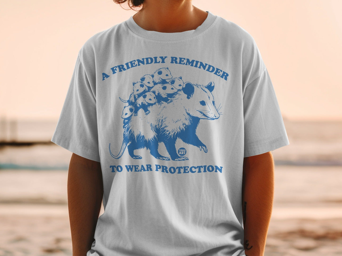 White t-shirt with blue graphic of a possum with babies, "A Friendly Reminder To Wear Protection" text.