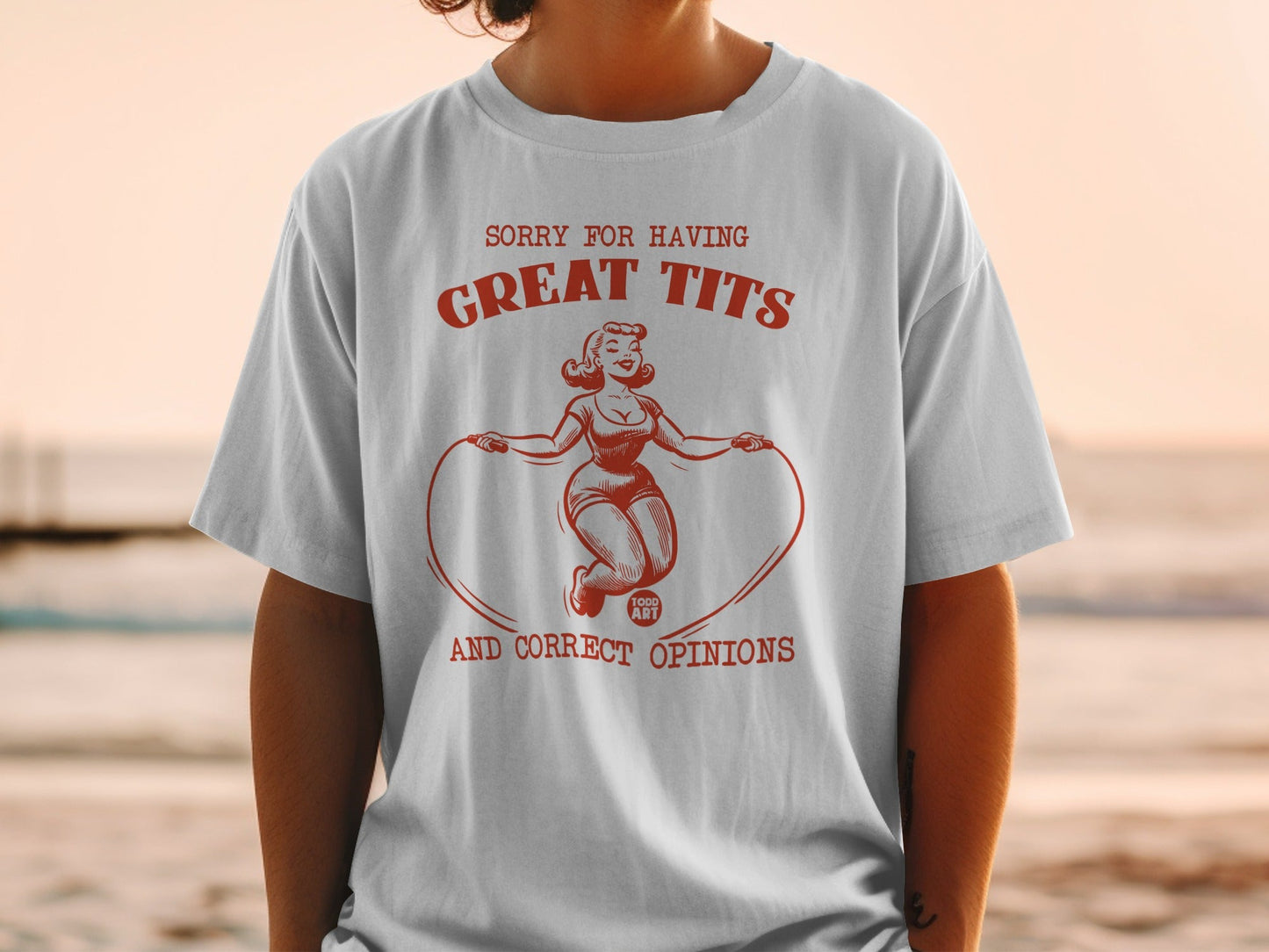 White t-shirt with red graphic of woman jumping rope, text reads "Sorry for having great tits and correct opinions".