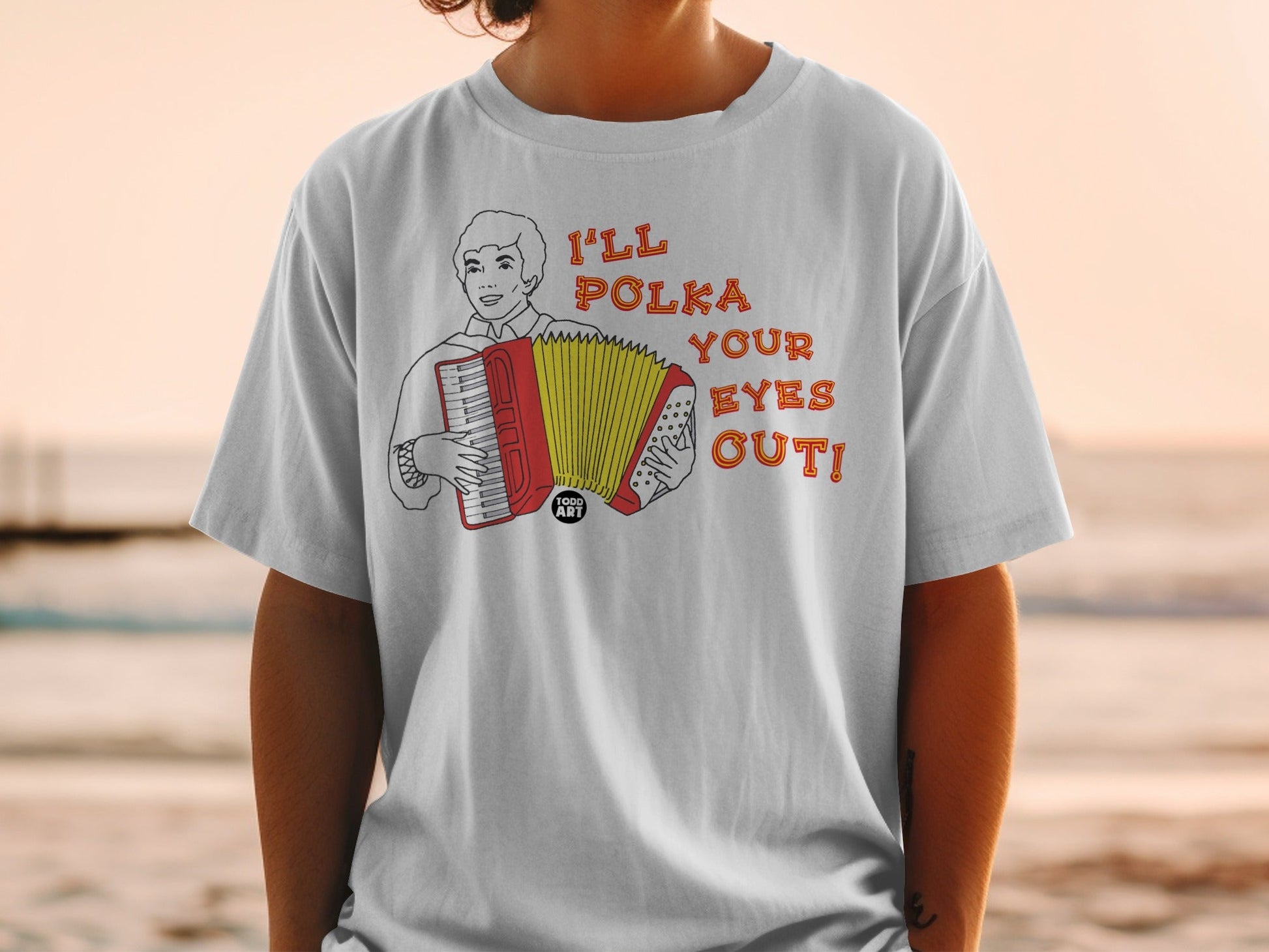 White t-shirt with graphic of a man playing accordion and text "I'LL POLKA YOUR EYES OUT!".