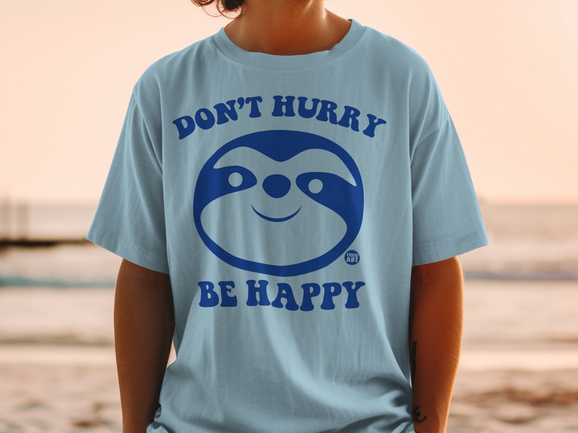 Light blue t-shirt with "DON'T HURRY BE HAPPY" and a smiling sloth graphic.