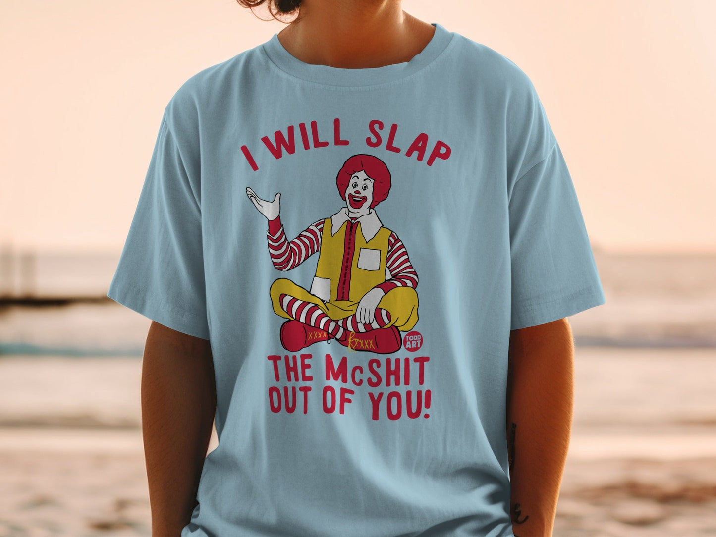 Ronald McDonald sitting cross-legged on a light blue t-shirt with text.