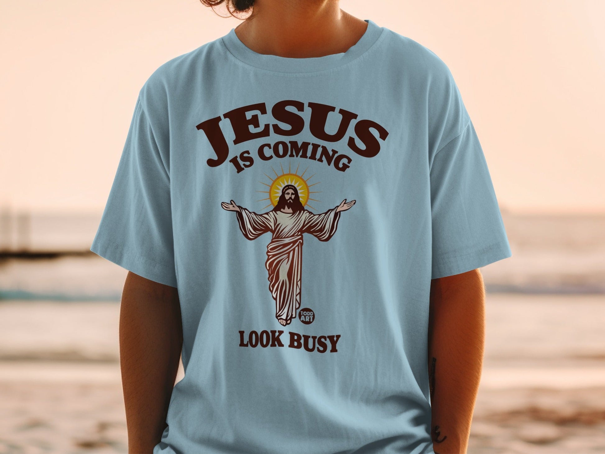 Light blue t-shirt with "JESUS IS COMING LOOK BUSY" text and Jesus illustration.
