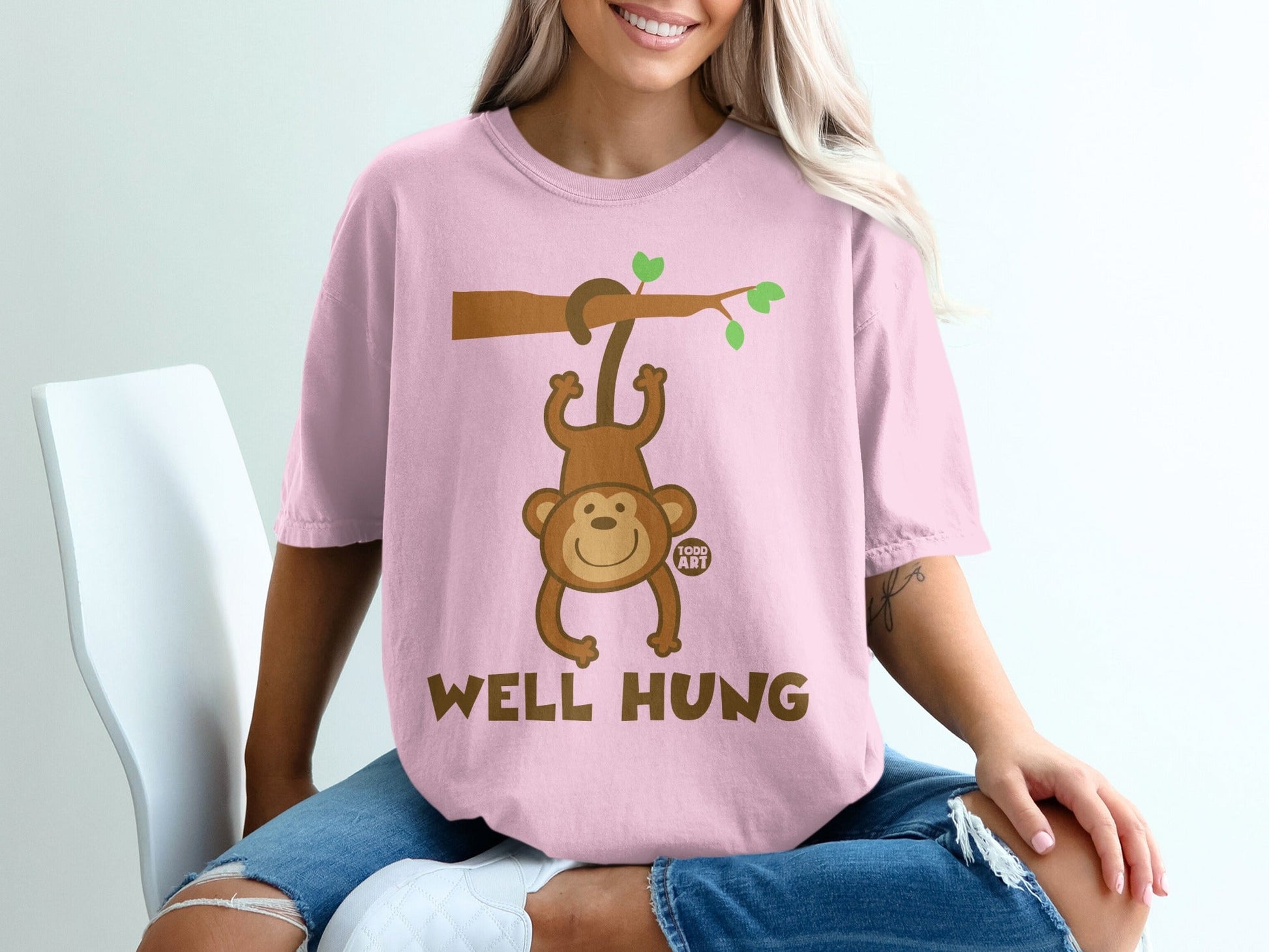 Pink t-shirt with a cartoon monkey hanging from a branch with text "WELL HUNG".