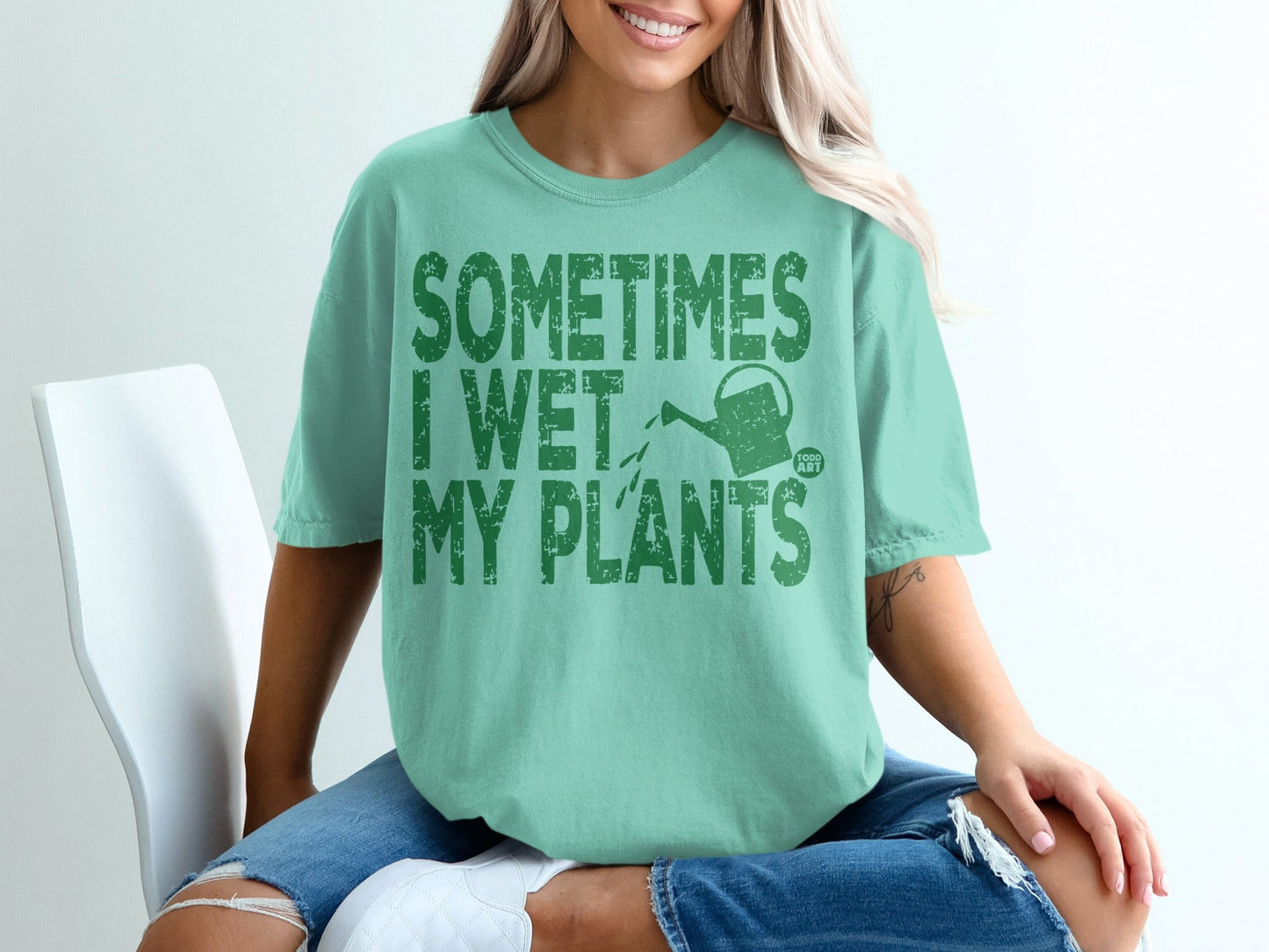 Green t-shirt with text "SOMETIMES I WET MY PLANTS" and a watering can.