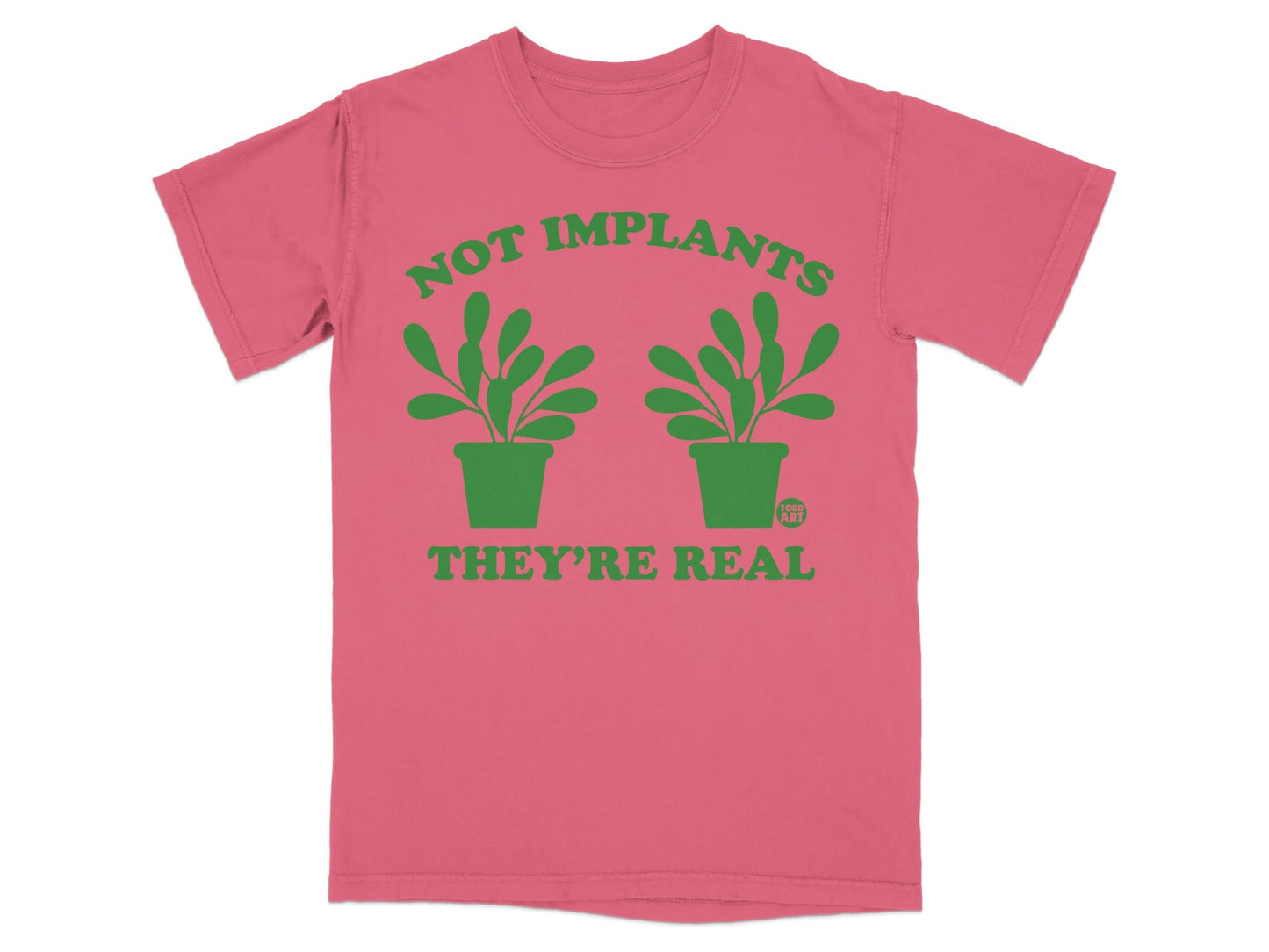 Pink t-shirt with green text "NOT IMPLANTS THEY'RE REAL" and two potted plants.