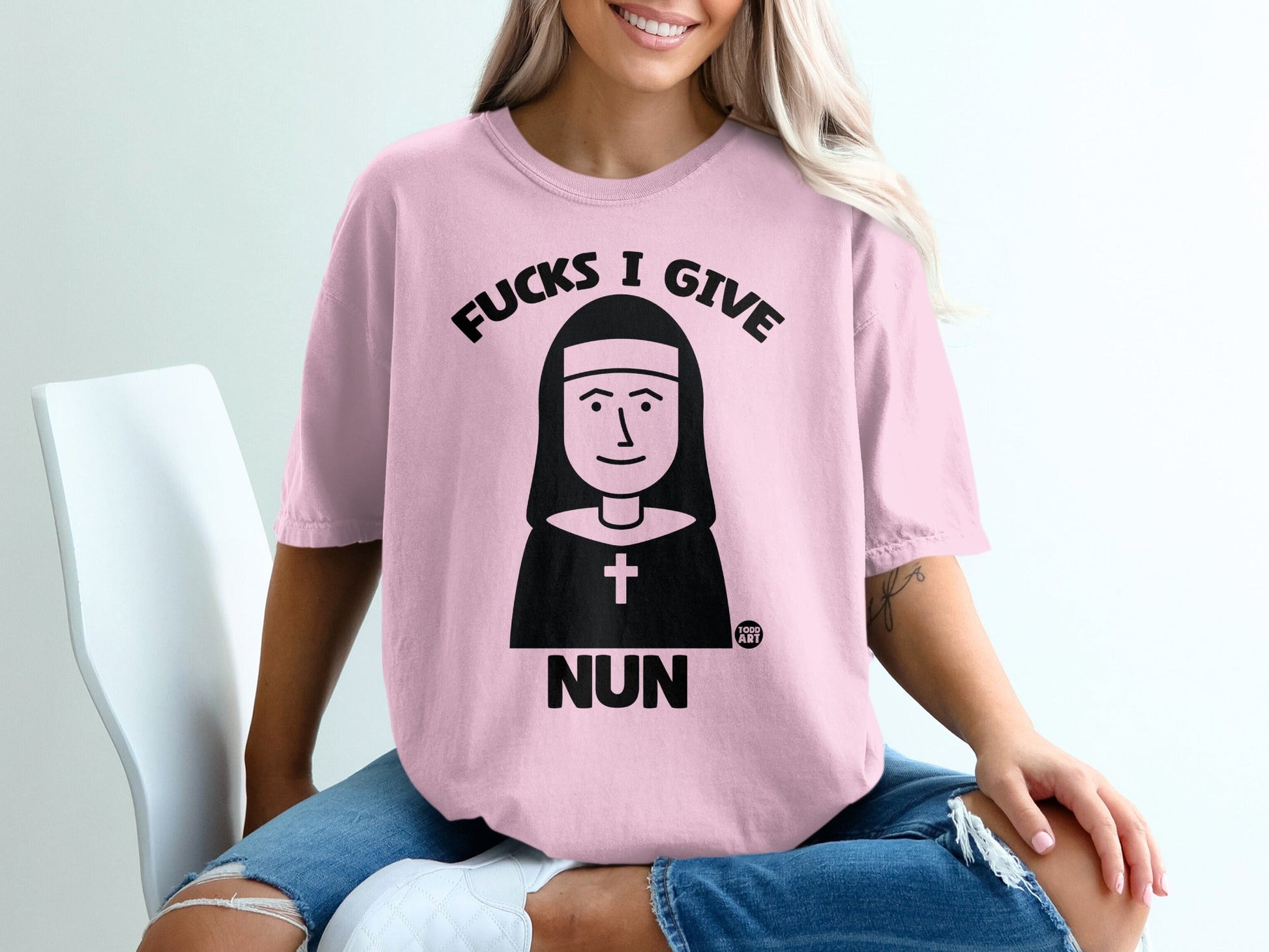 Pink t-shirt with "Fucks I Give Nun" graphic on a seated person.