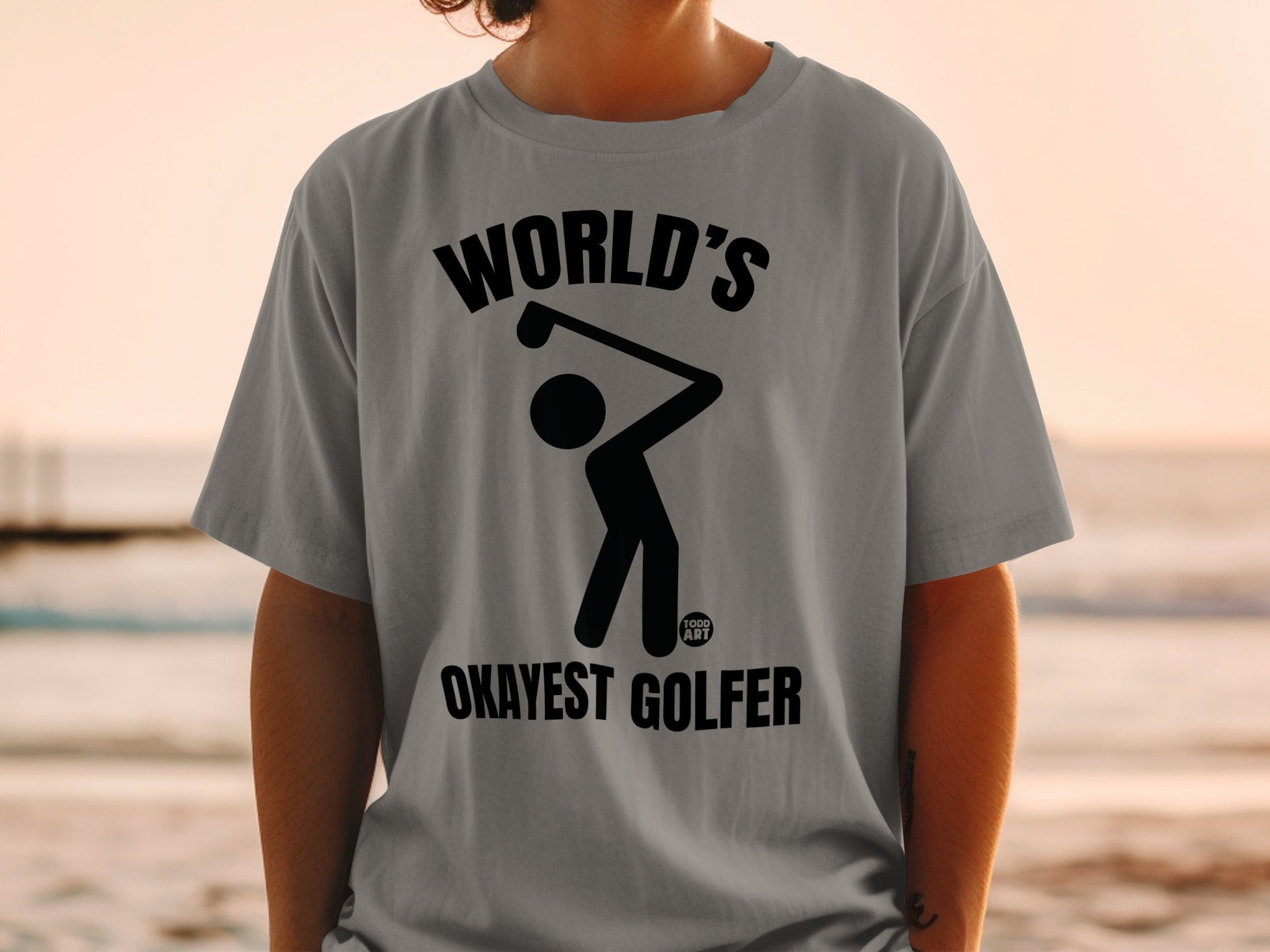 Gray t-shirt with "WORLD'S OKAYEST GOLFER" text and a stick figure golfer graphic.