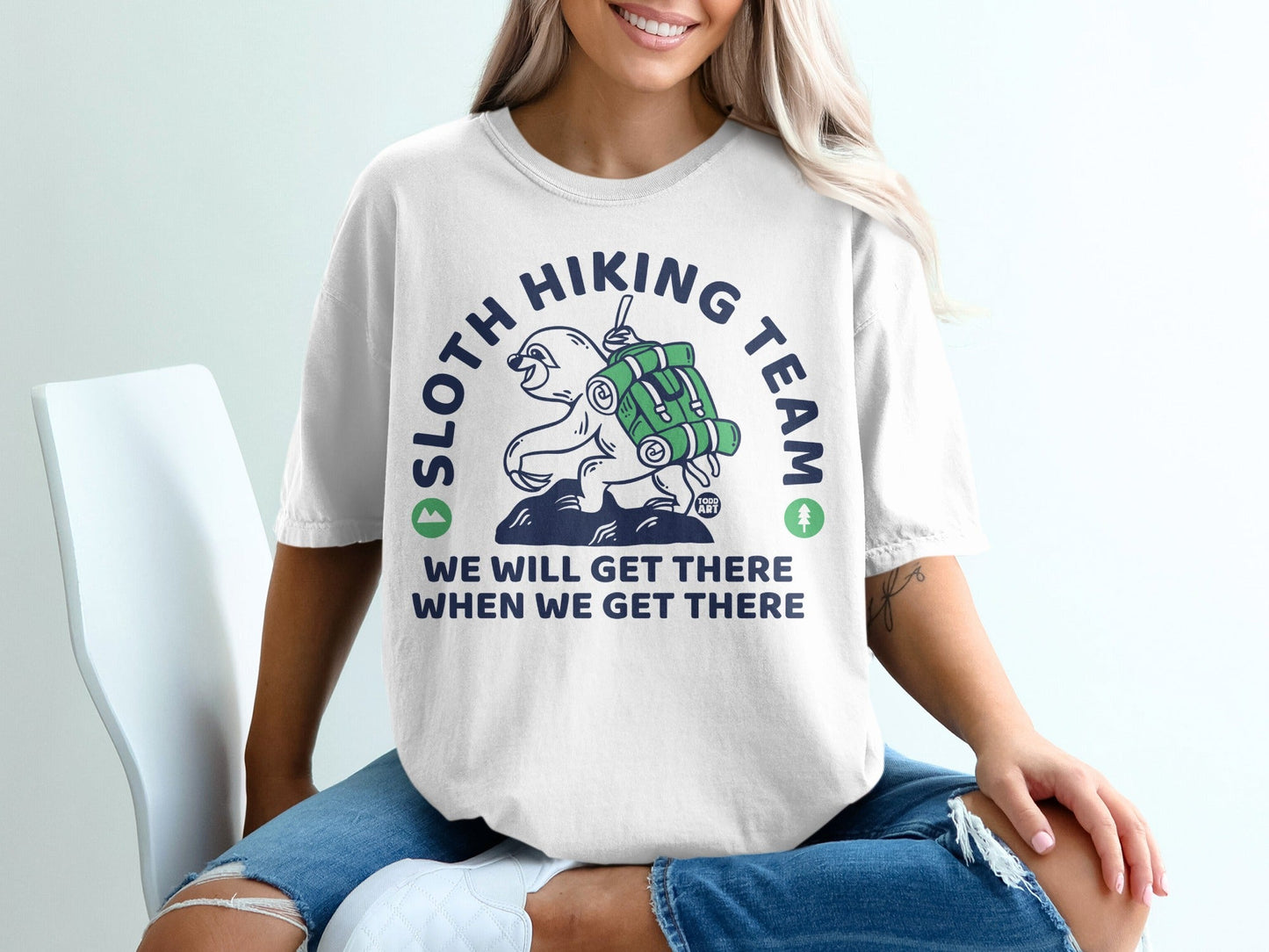 White t-shirt with graphic of a sloth hiking and text "SLOTH HIKING TEAM WE WILL GET THERE WHEN WE GET THERE".