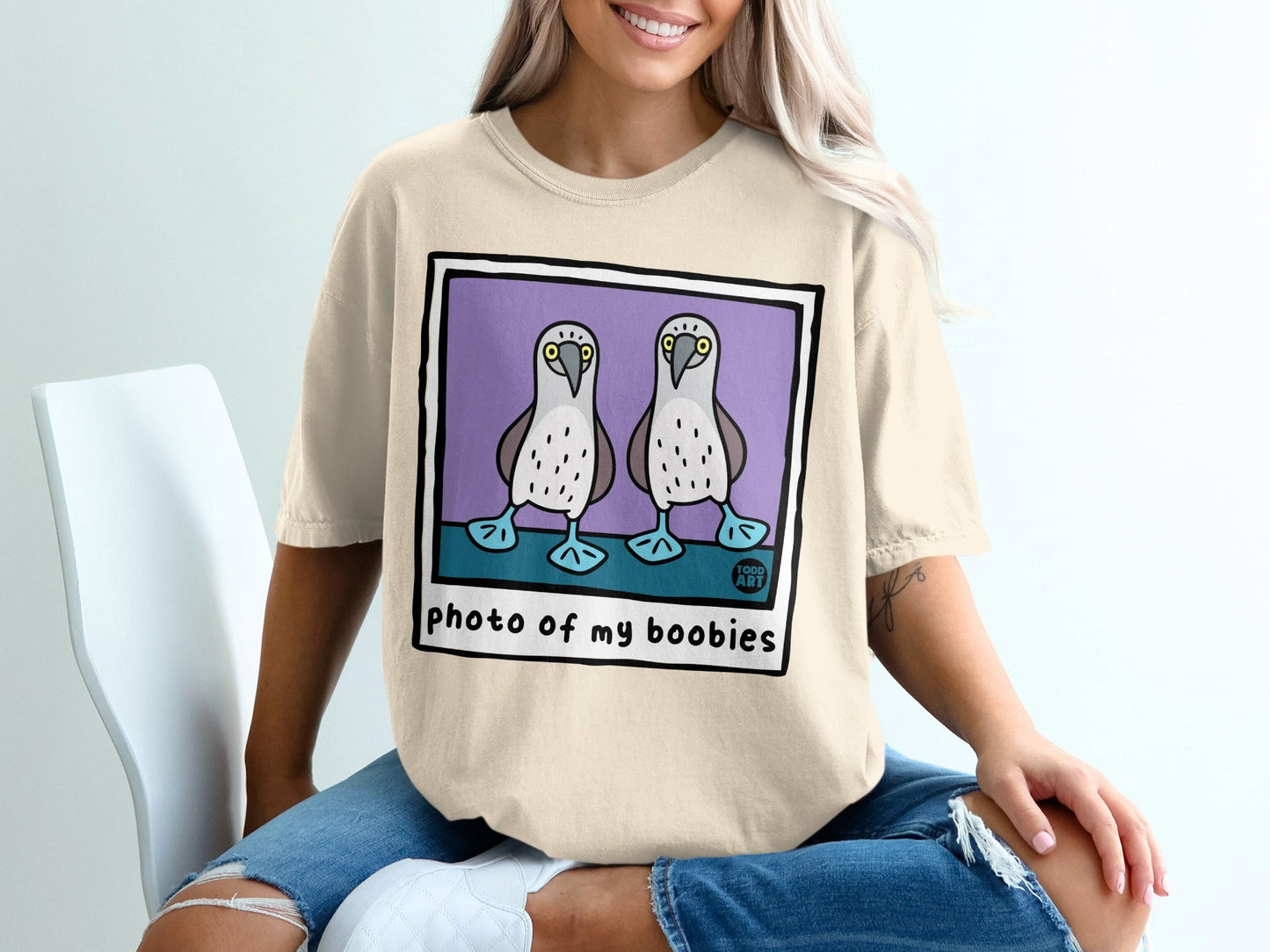T-shirt featuring a cartoon illustration of two boobies in a purple square with text.