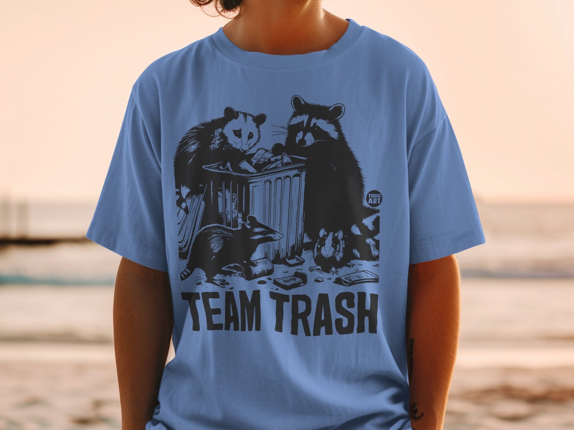 Blue t-shirt with "TEAM TRASH" text and raccoons and opossum rummaging in a trash can.