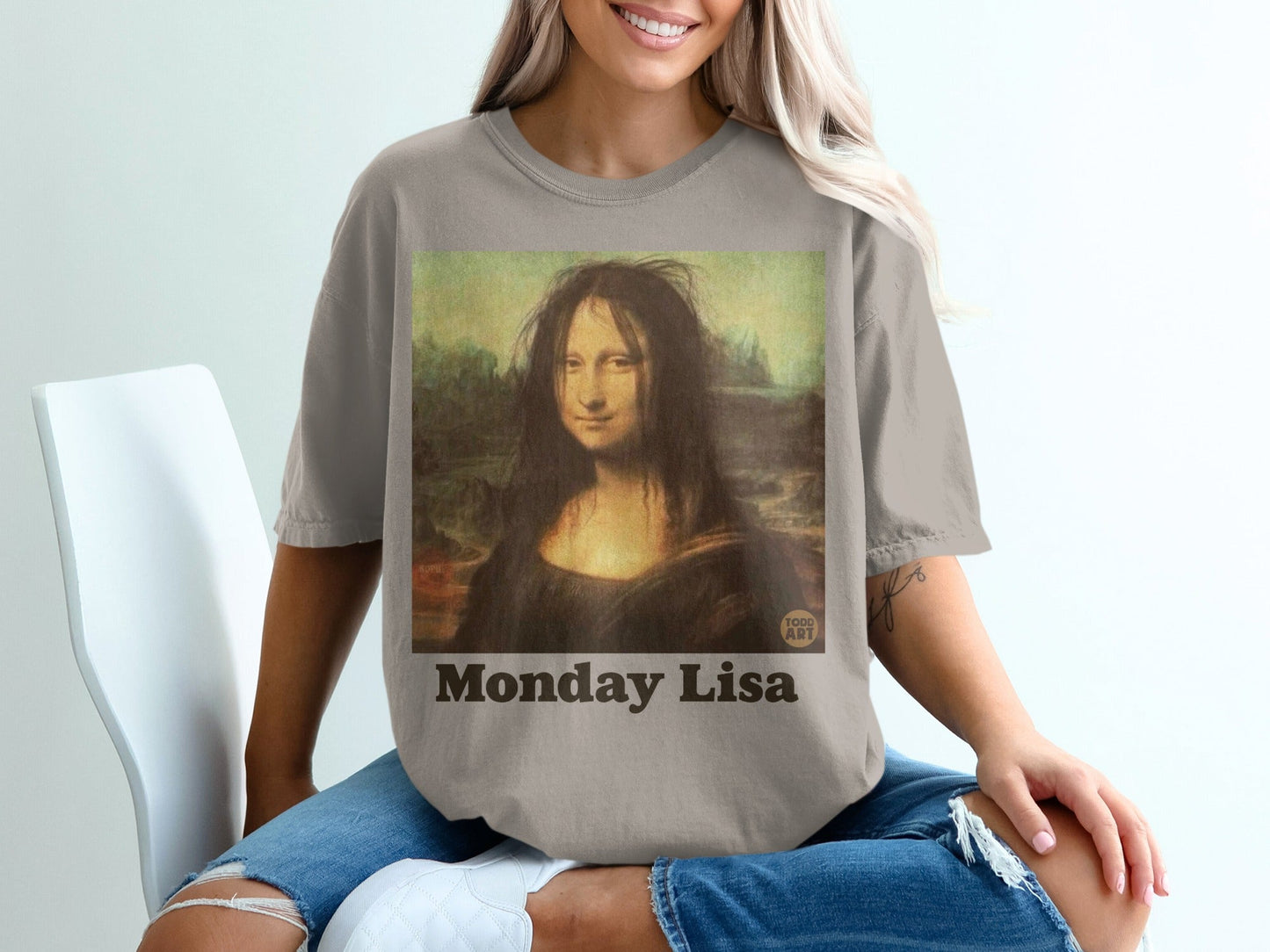 Mon√° Lisa painting with messy hair, text "Monday Lisa" on a taupe t-shirt.