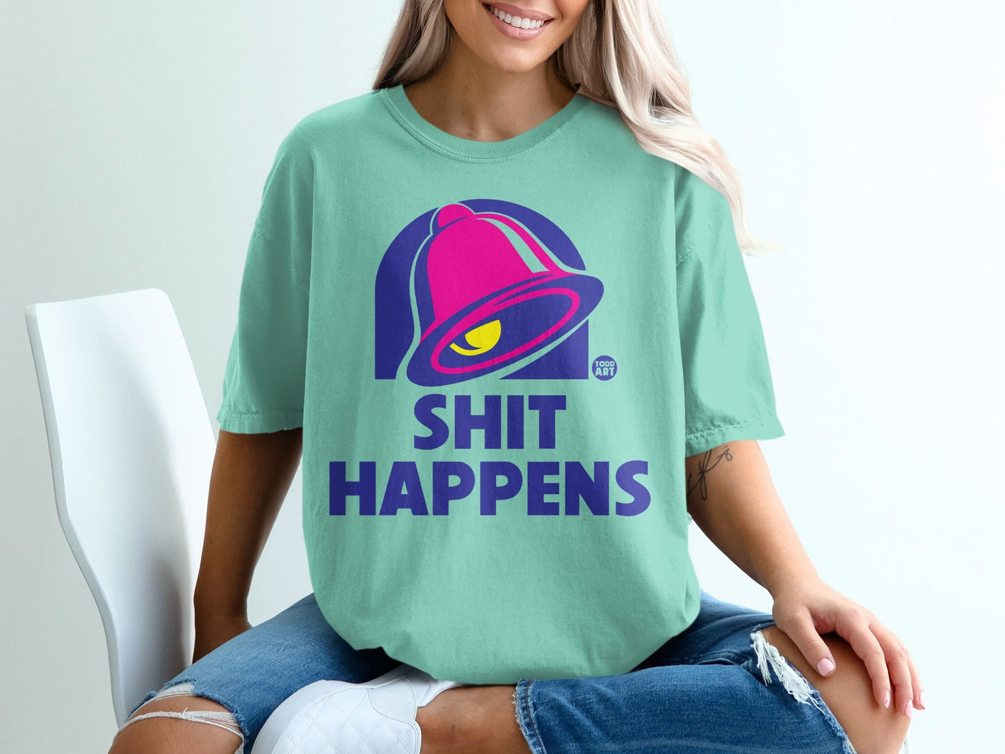 Aqua t-shirt with purple Taco Bell-inspired bell logo and "SHIT HAPPENS" text.