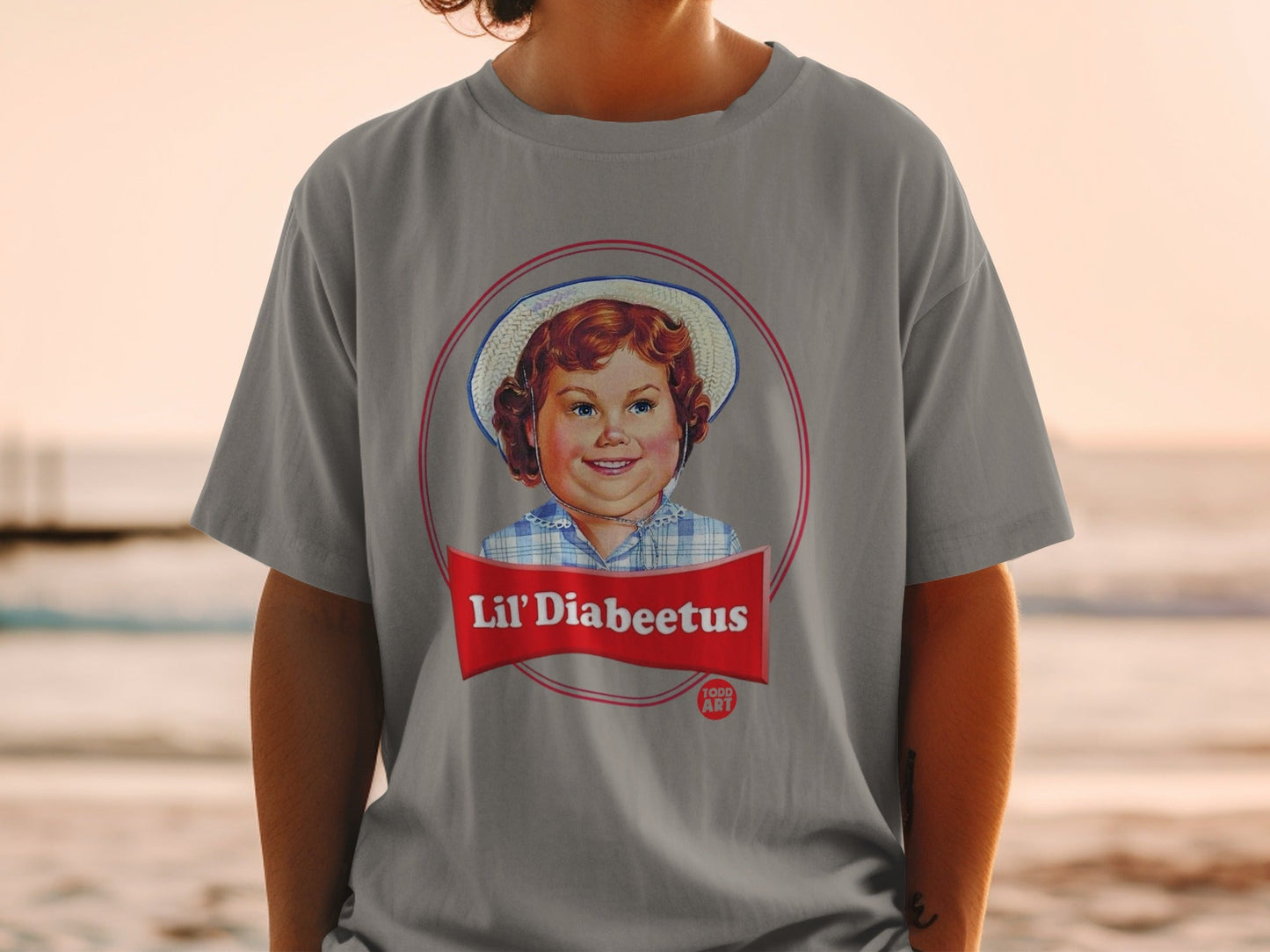 Lil' Diabeetus logo featuring a smiling child in a hat on a grey t-shirt.