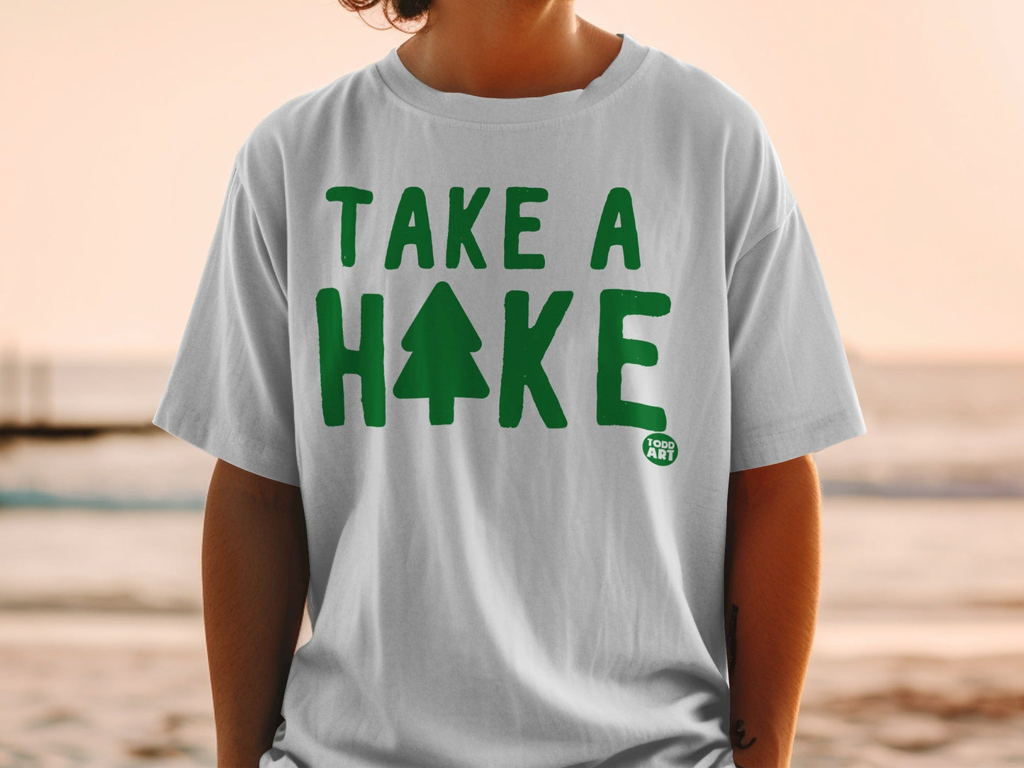White t-shirt with green text "TAKE A HIKE" and a small tree logo.