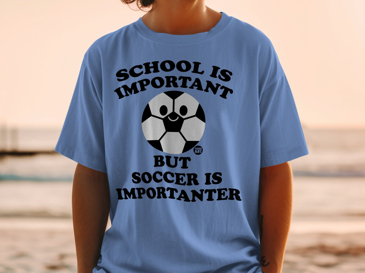 Blue t-shirt with a soccer ball graphic and text: School is important, but soccer is importanter.