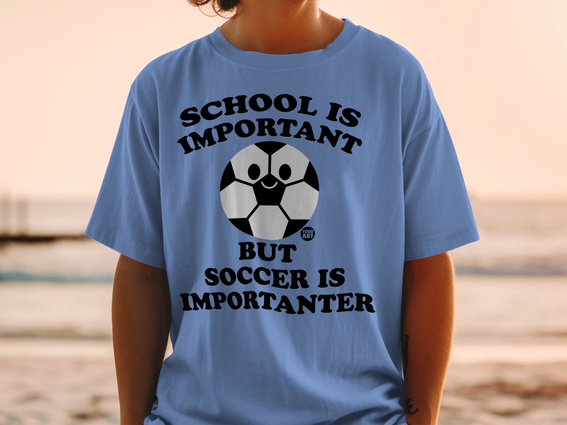 Blue t-shirt with a soccer ball graphic and text: School is important, but soccer is importanter.