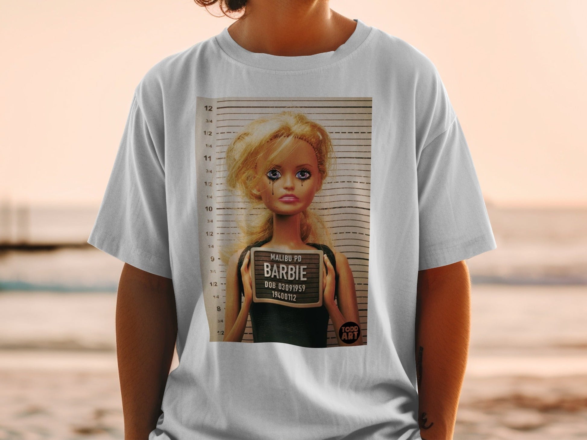 Barbie mugshot with "MALIBU PD" and DOB on a white t-shirt.