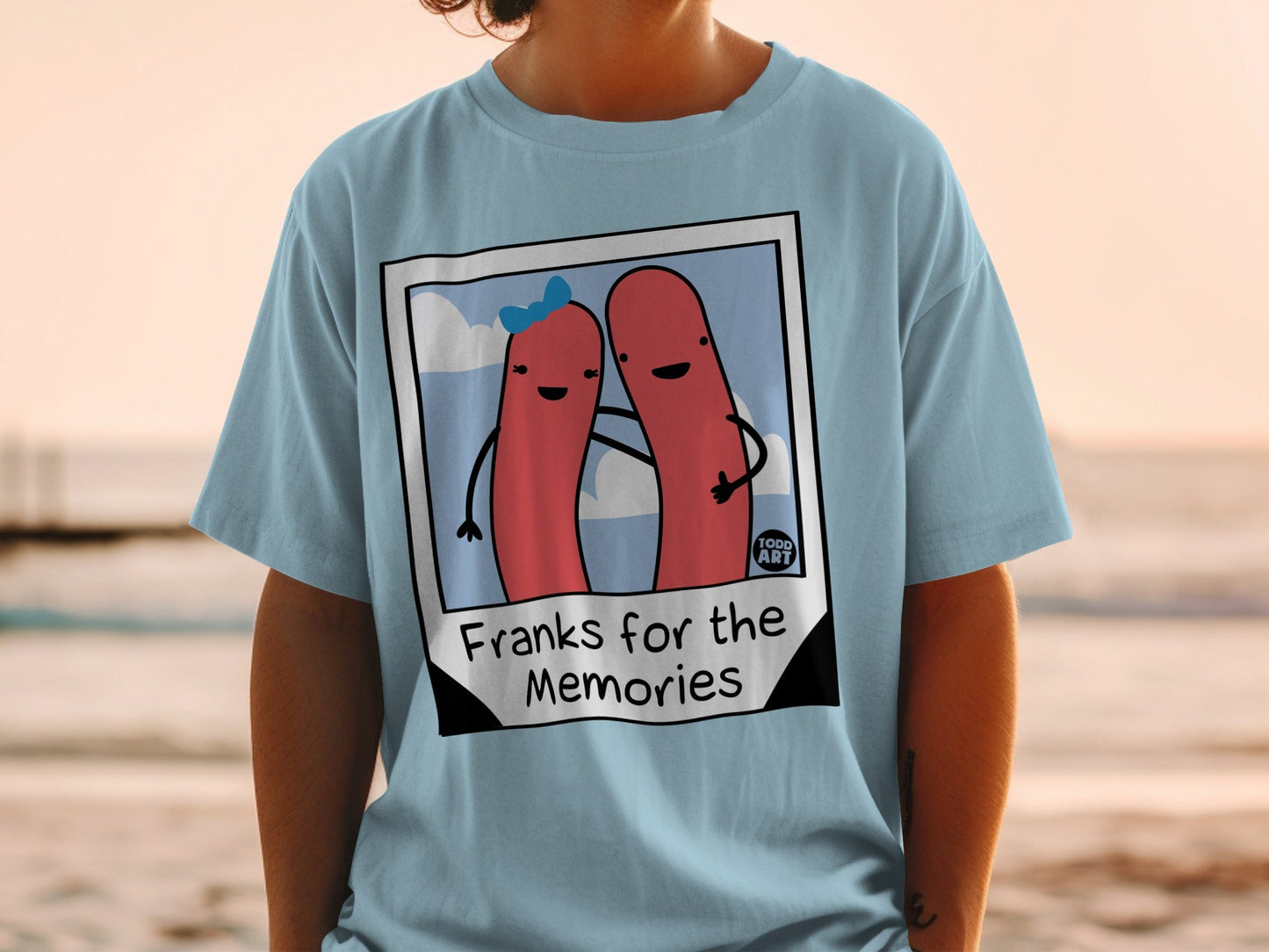 Light blue t-shirt with cartoon hot dogs in a photo frame, text "Franks for the Memories".
