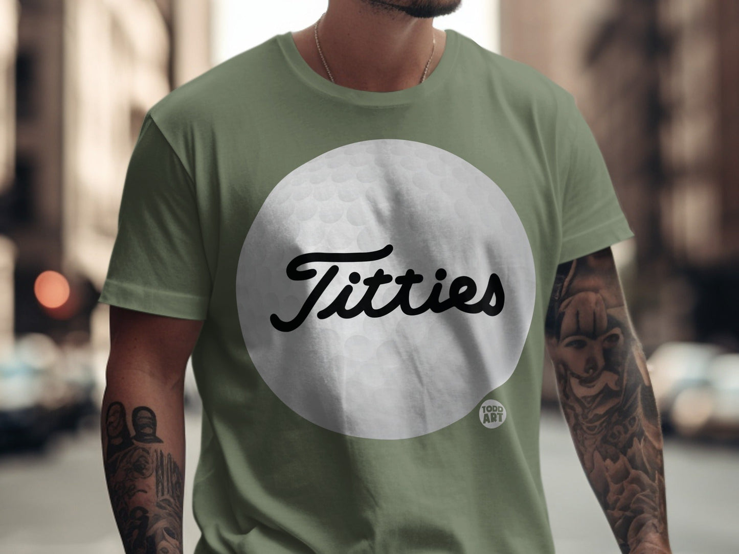 Green t-shirt with "Titties" in cursive on a golf ball graphic.