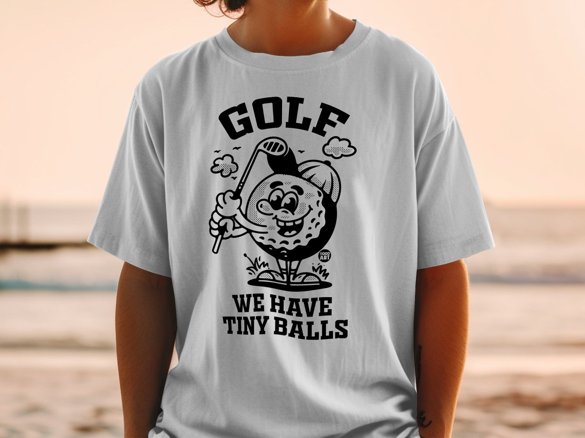 T-shirt graphic of a smiling golf ball character with a golf club.