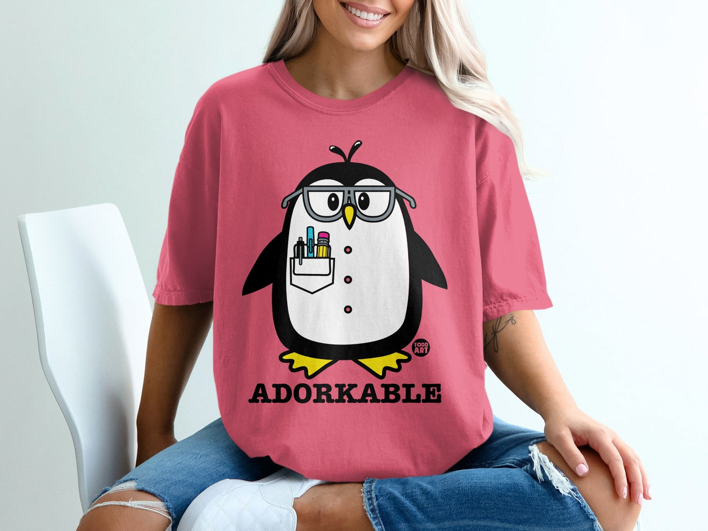 Pink t-shirt with a cartoon penguin wearing glasses and holding art supplies.