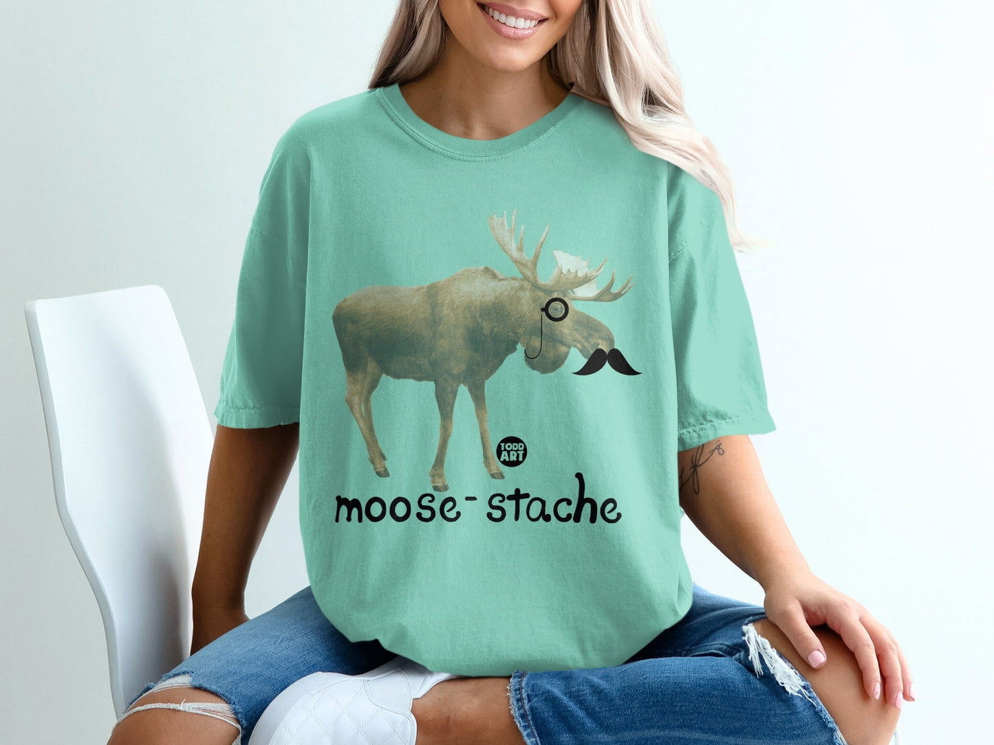 Moose with monocle and mustache, text "moose-stache" below.