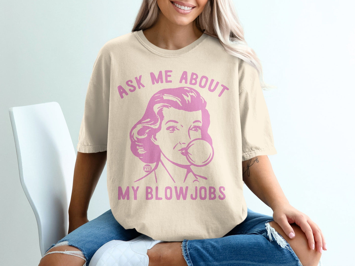 Cream t-shirt with pink graphic of a woman blowing bubblegum, text reads "ASK ME ABOUT MY BLOW JOBS".