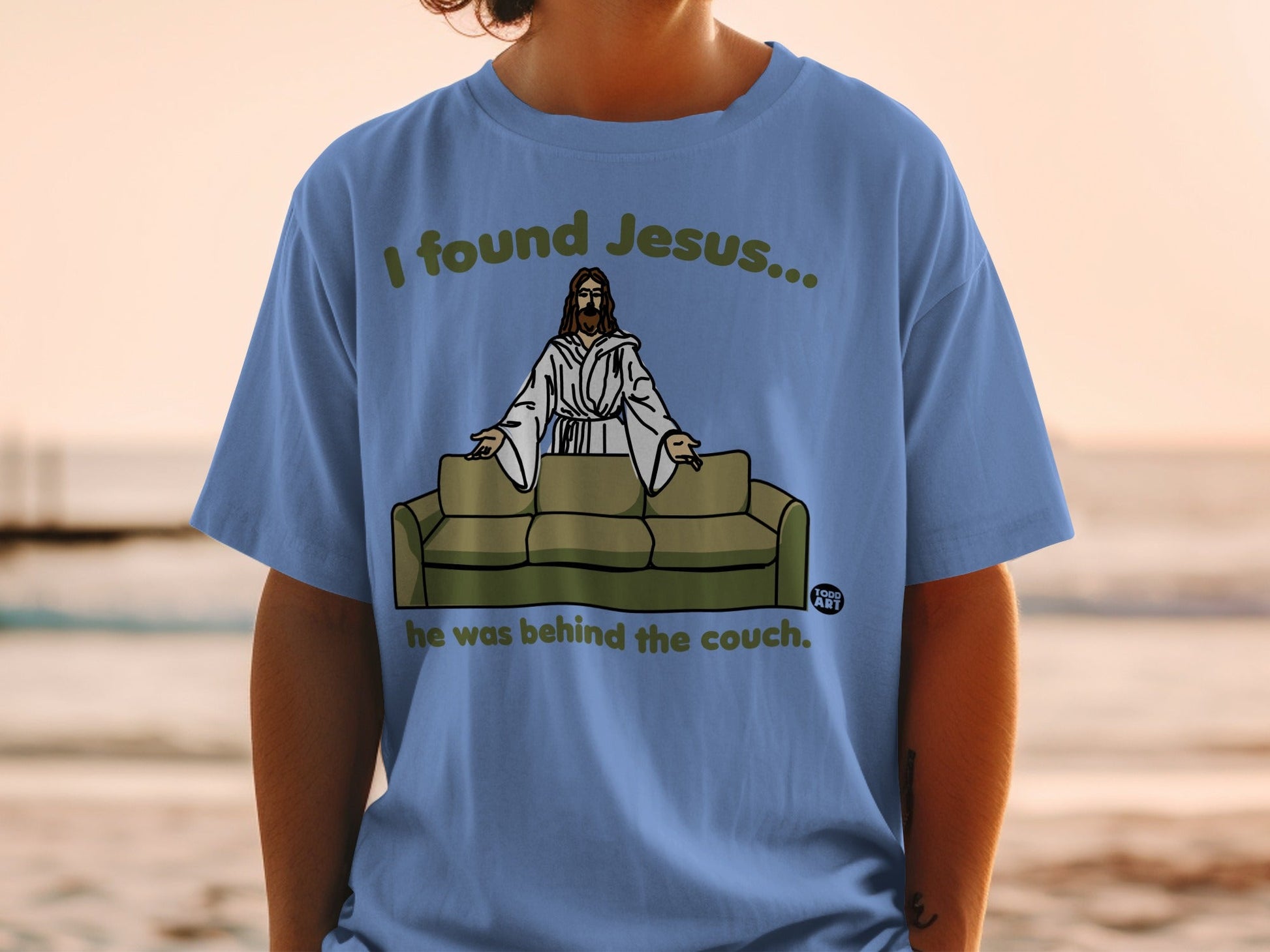Blue t-shirt with "I found Jesus... he was behind the couch." text.