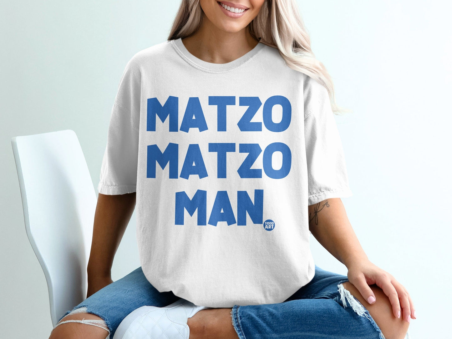 White t-shirt with blue text "MATZO MATZO MAN" and a small "1000 ART" logo.