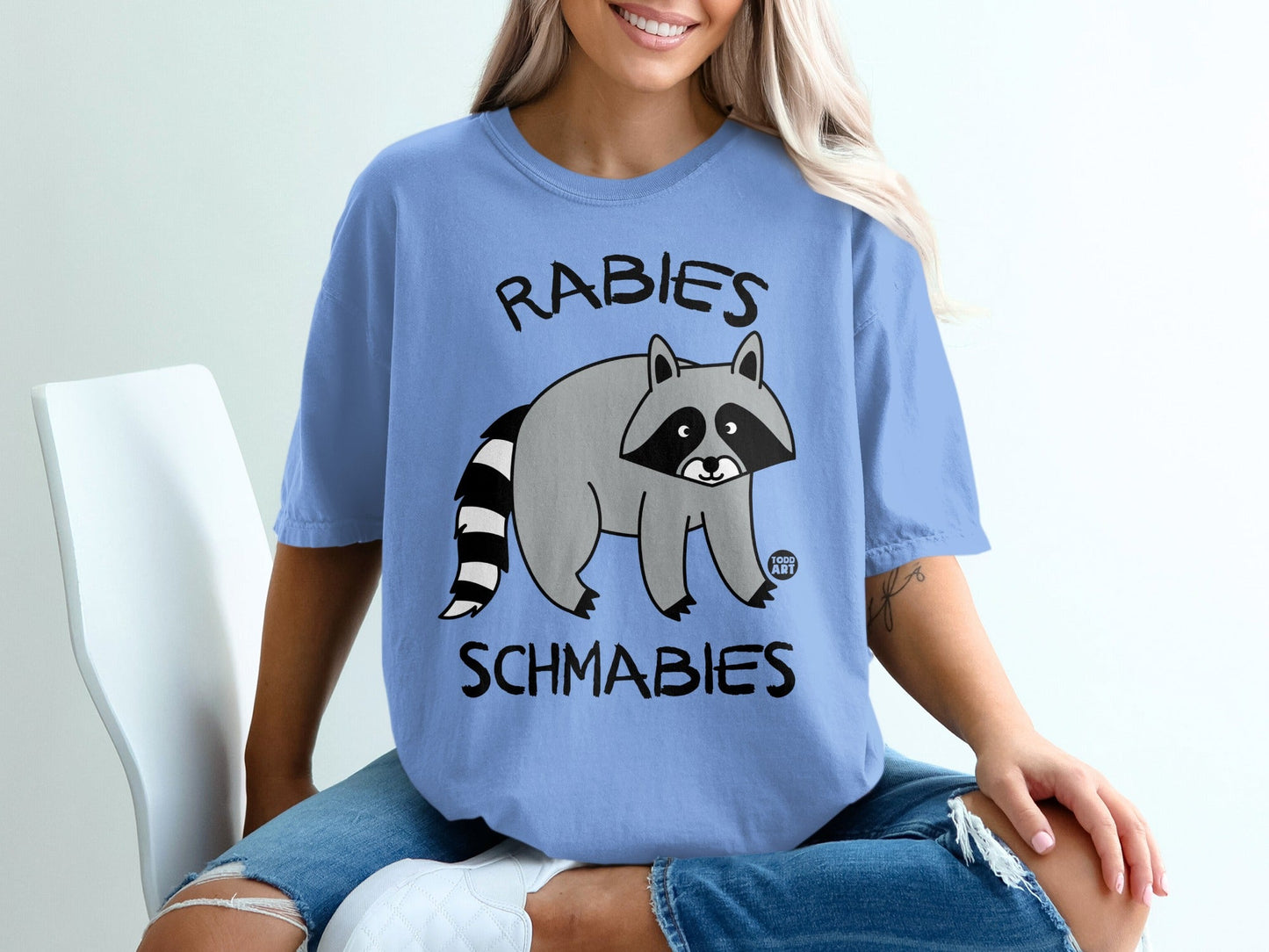 Blue t-shirt with "Rabies Schmabies" text and cartoon raccoon graphic.