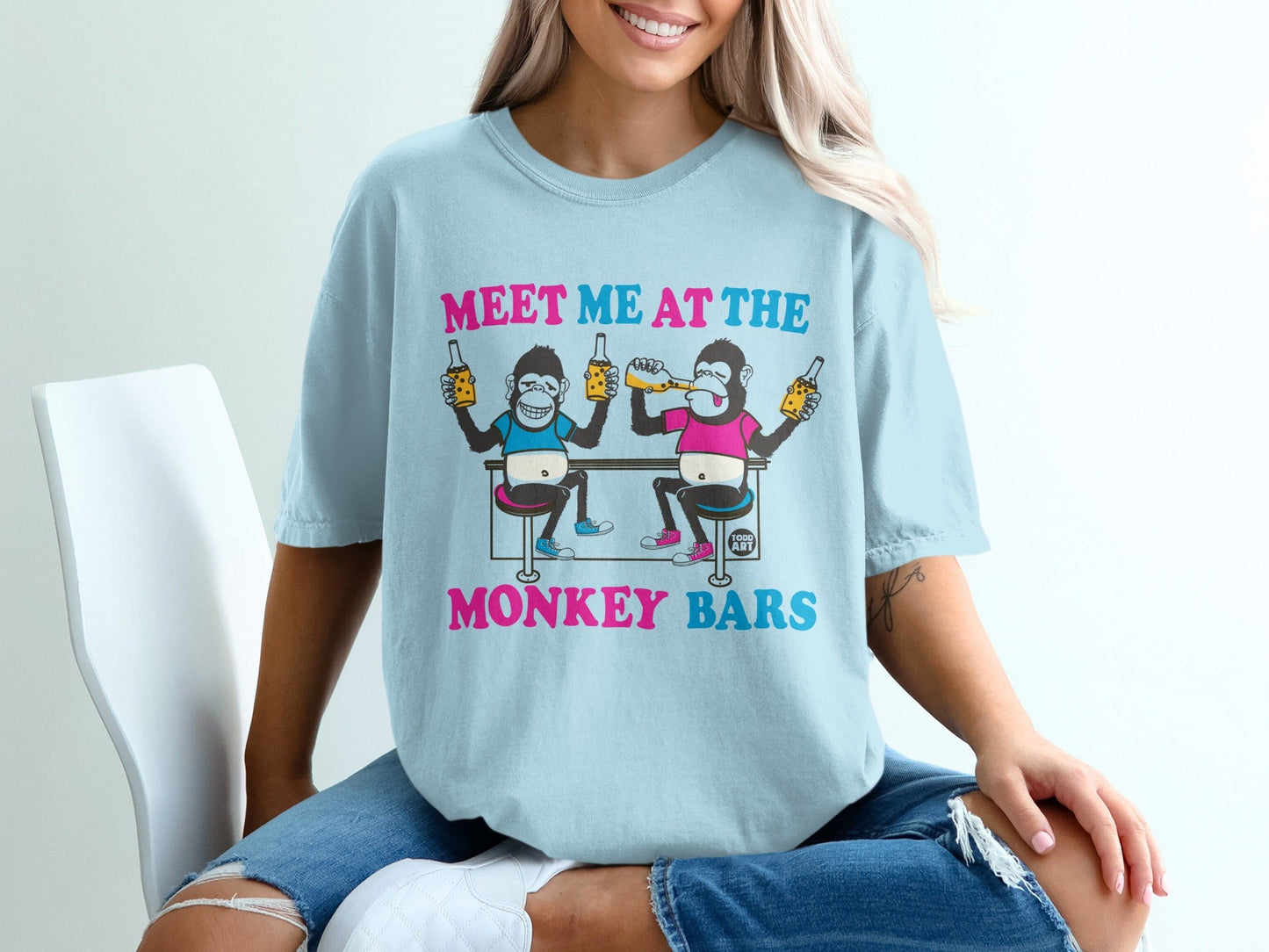Light blue t-shirt with cartoon monkeys drinking on a bar stool.