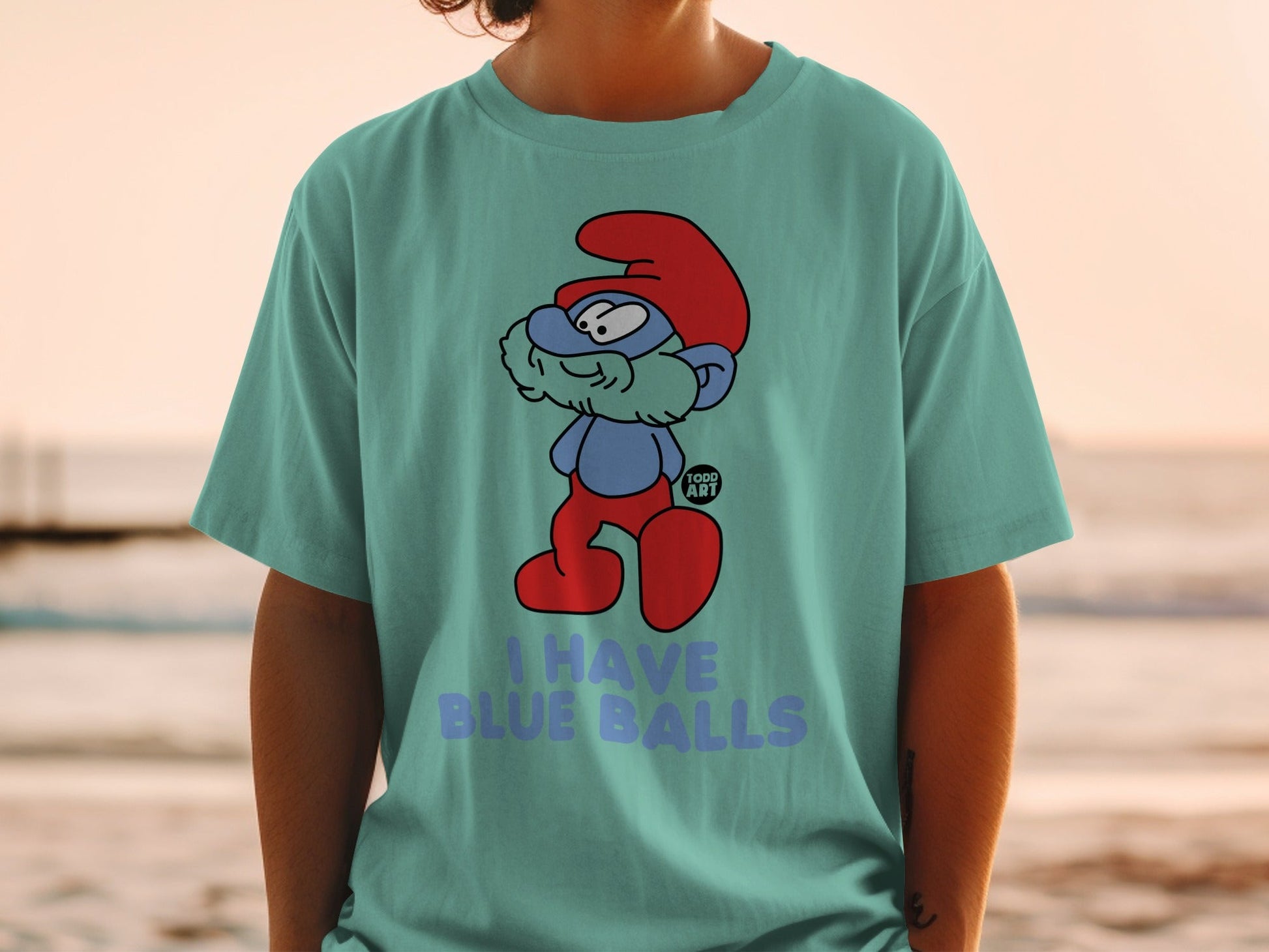 Smurf character wearing a red hat and red pants on a blue t-shirt with text.