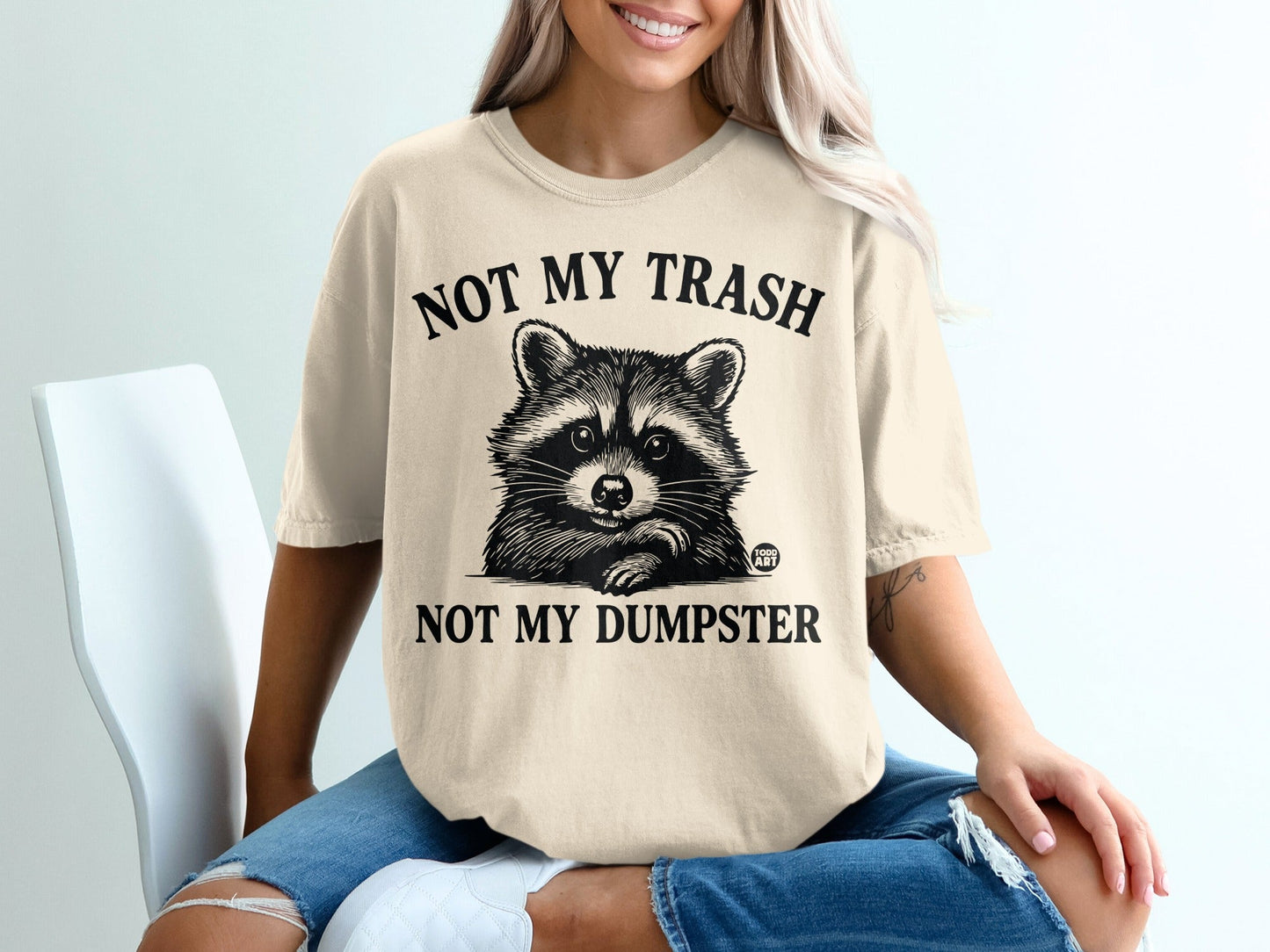 Cream t-shirt with raccoon graphic and text "NOT MY TRASH NOT MY DUMPSTER".