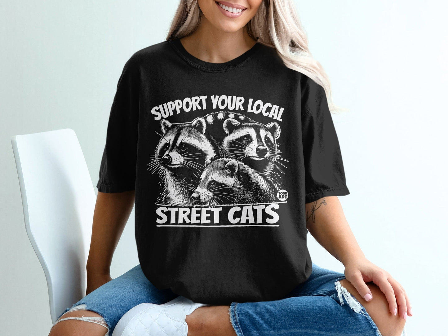 Black t-shirt with graphic of three raccoons and text "SUPPORT YOUR LOCAL STREET CATS".