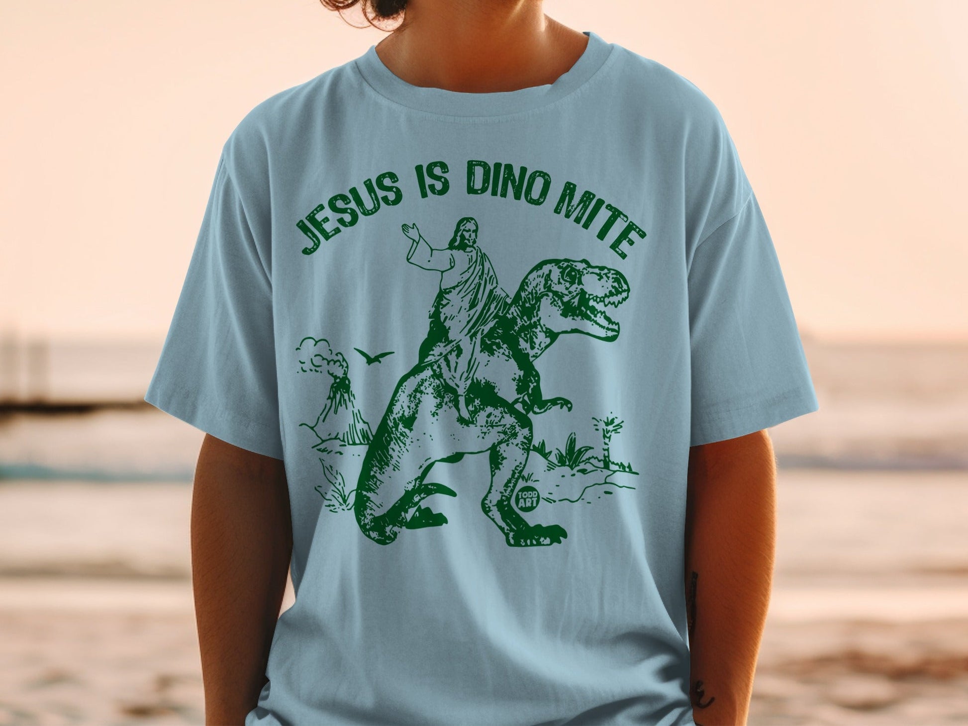 Light blue t-shirt with Jesus riding a T-Rex.