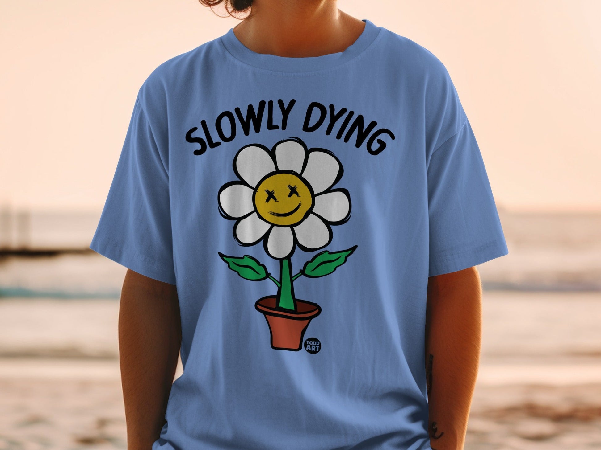 Blue t-shirt with a cartoon flower wearing sunglasses and text "SLOWLY DYING".