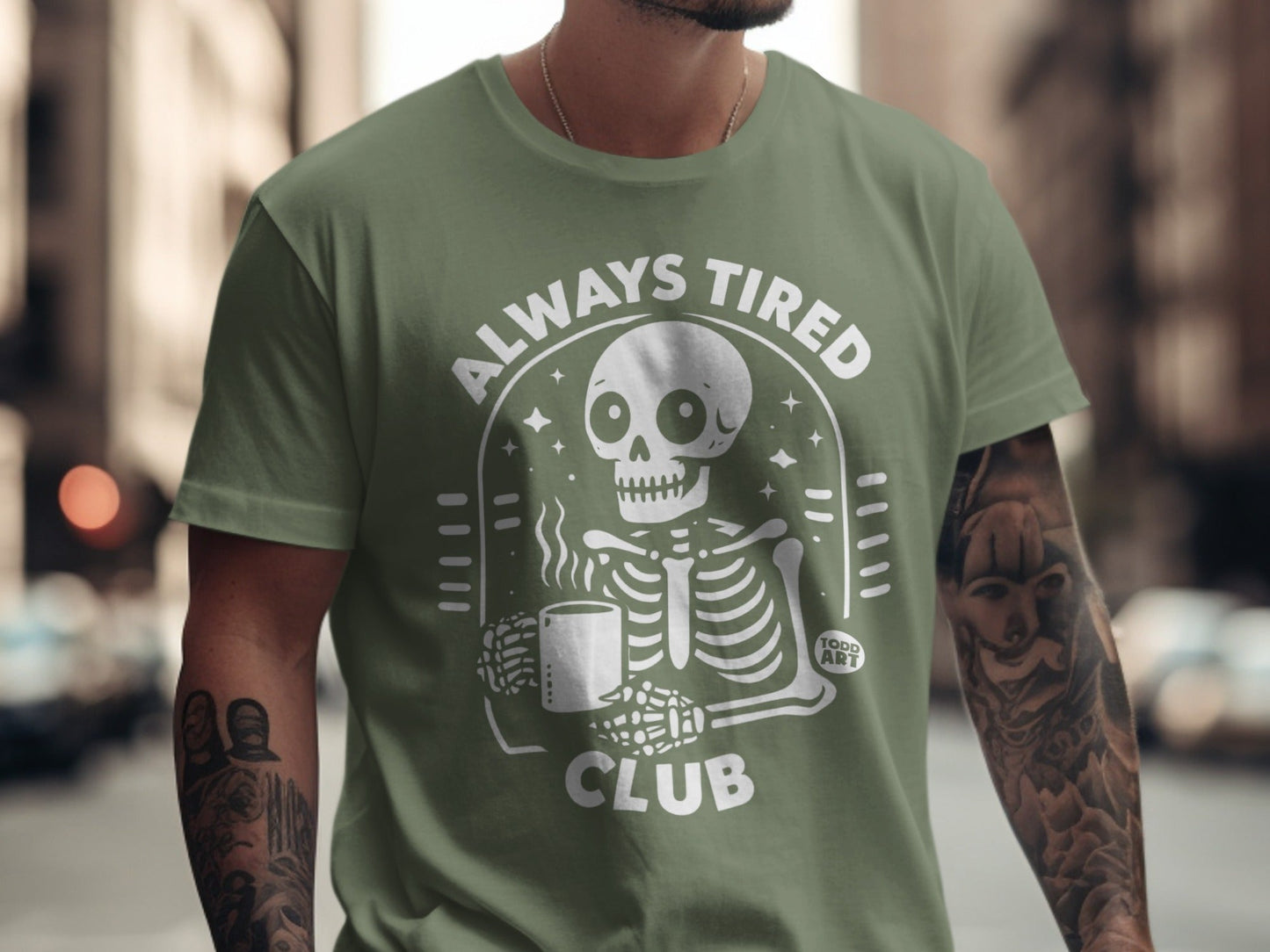 Green t-shirt with skeleton holding coffee mug, "Always Tired Club" text.