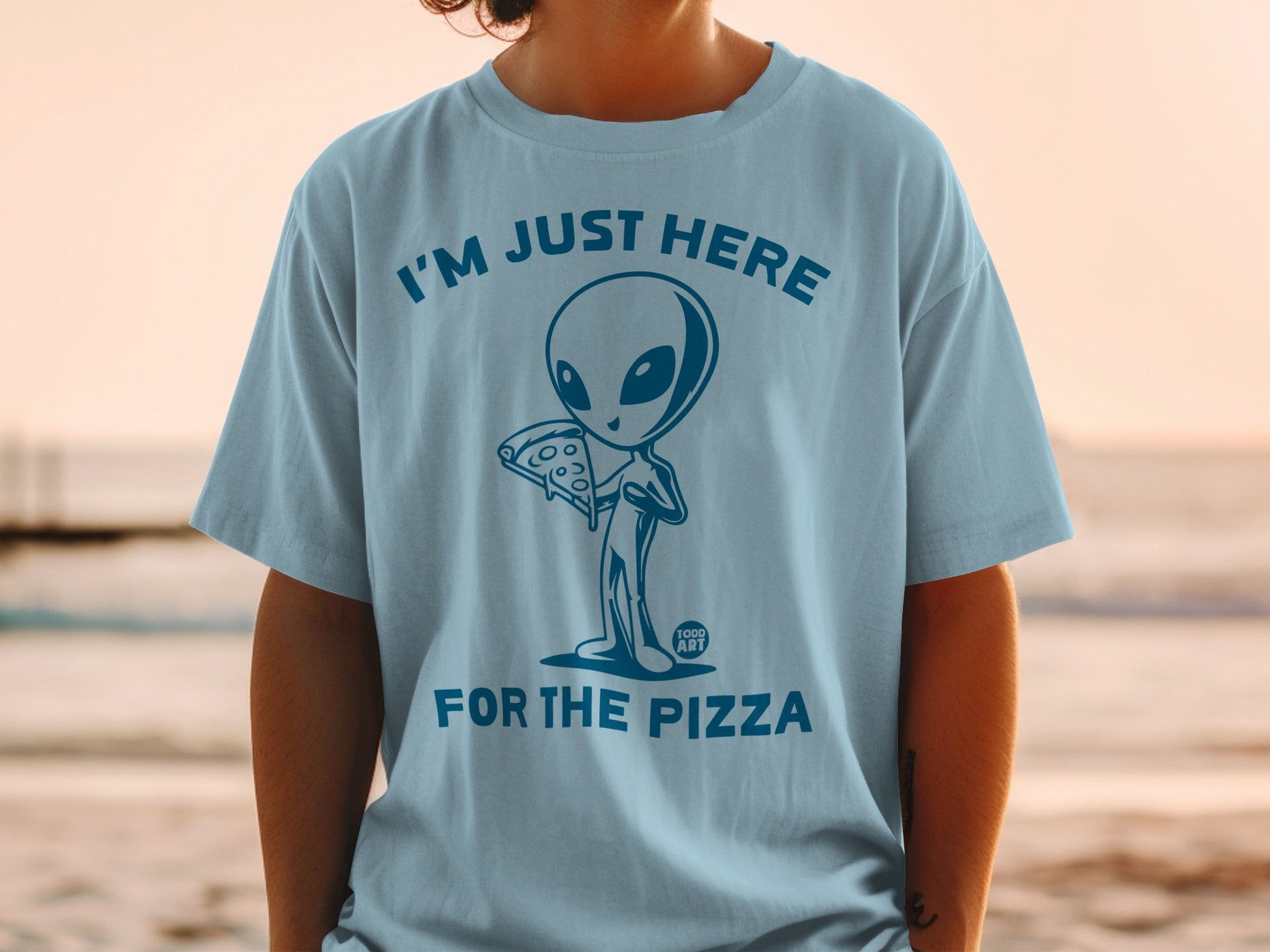 Light blue t-shirt with a cartoon alien holding pizza and text "I'M JUST HERE FOR THE PIZZA".