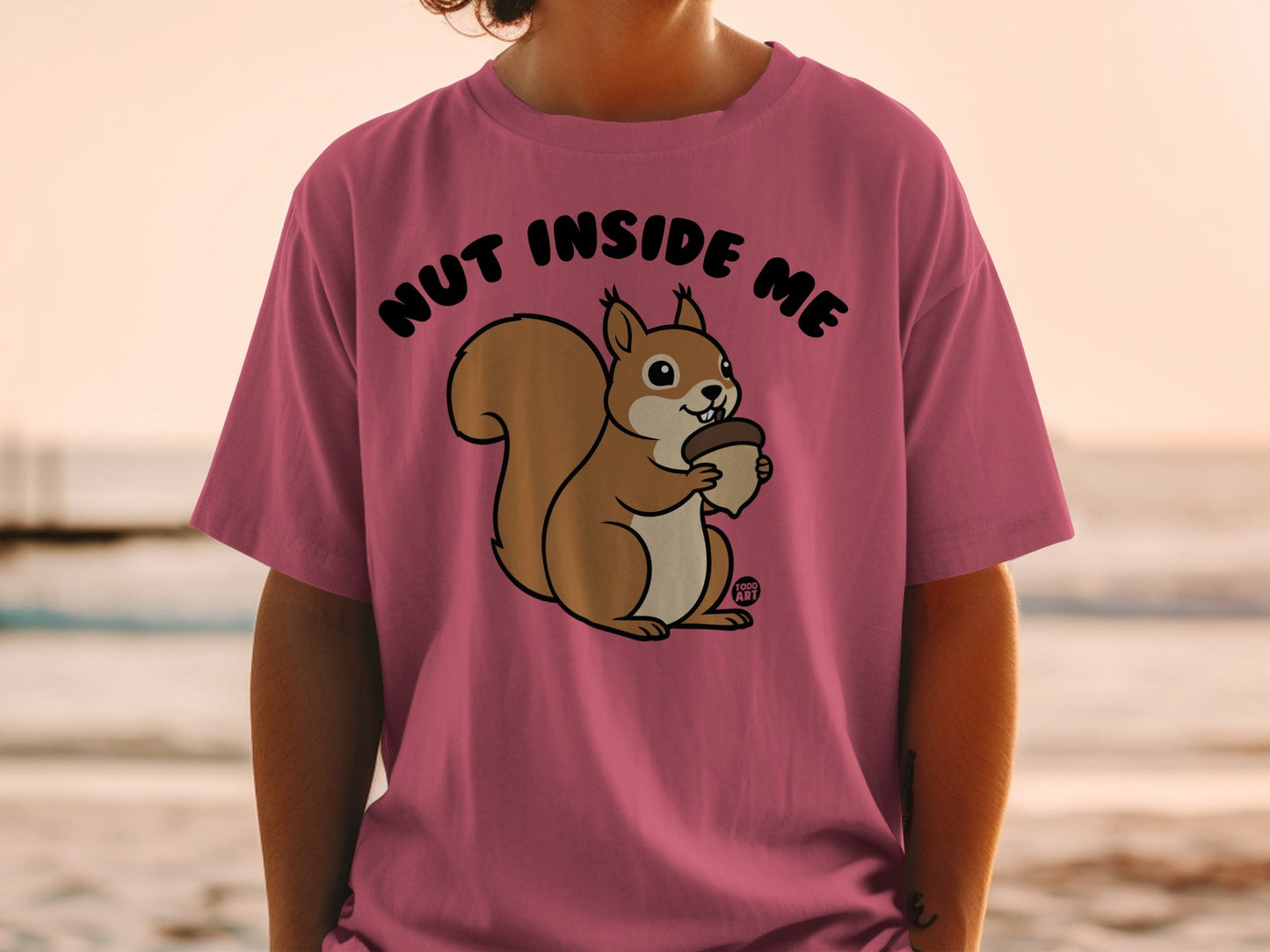 Pink t-shirt with cartoon squirrel holding an acorn and text "NUT INSIDE ME".