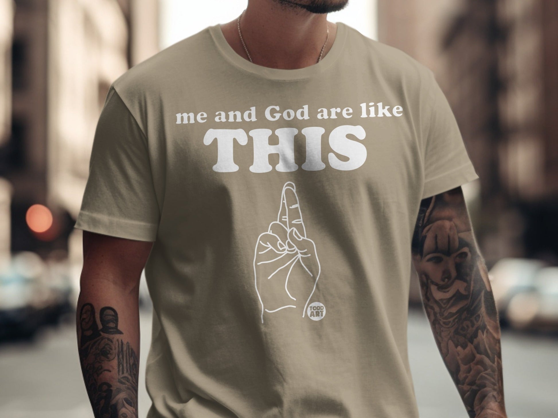 T-shirt with text "me and God are like THIS" and line art of two fingers crossed.