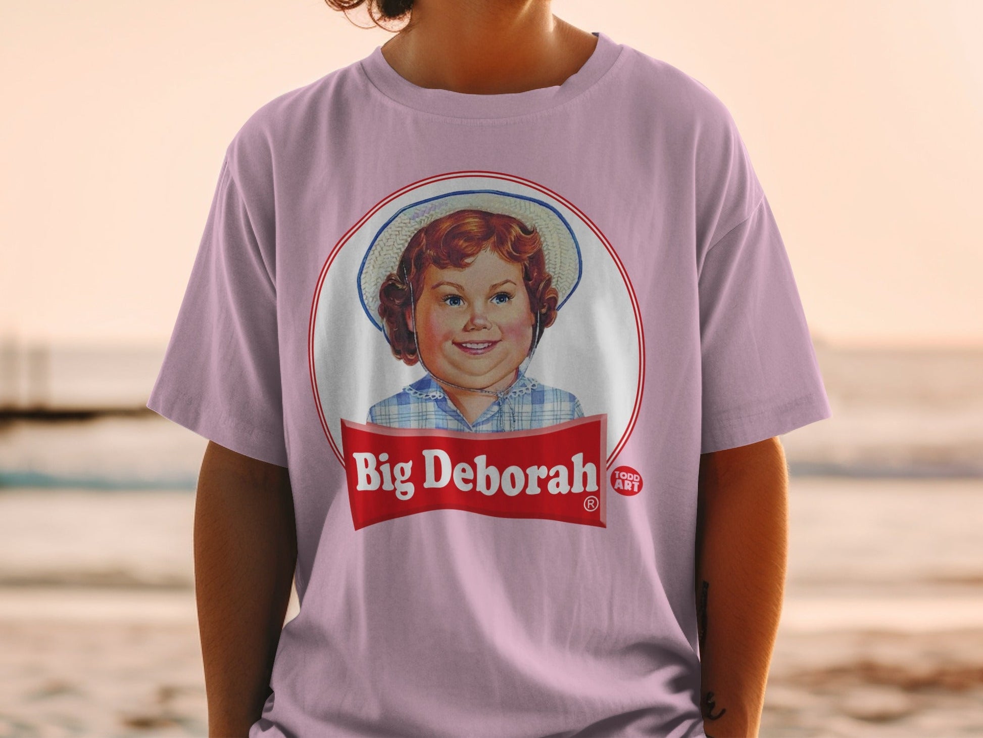 Pink t-shirt with a circular logo featuring a young girl and "Big Deborah" text.