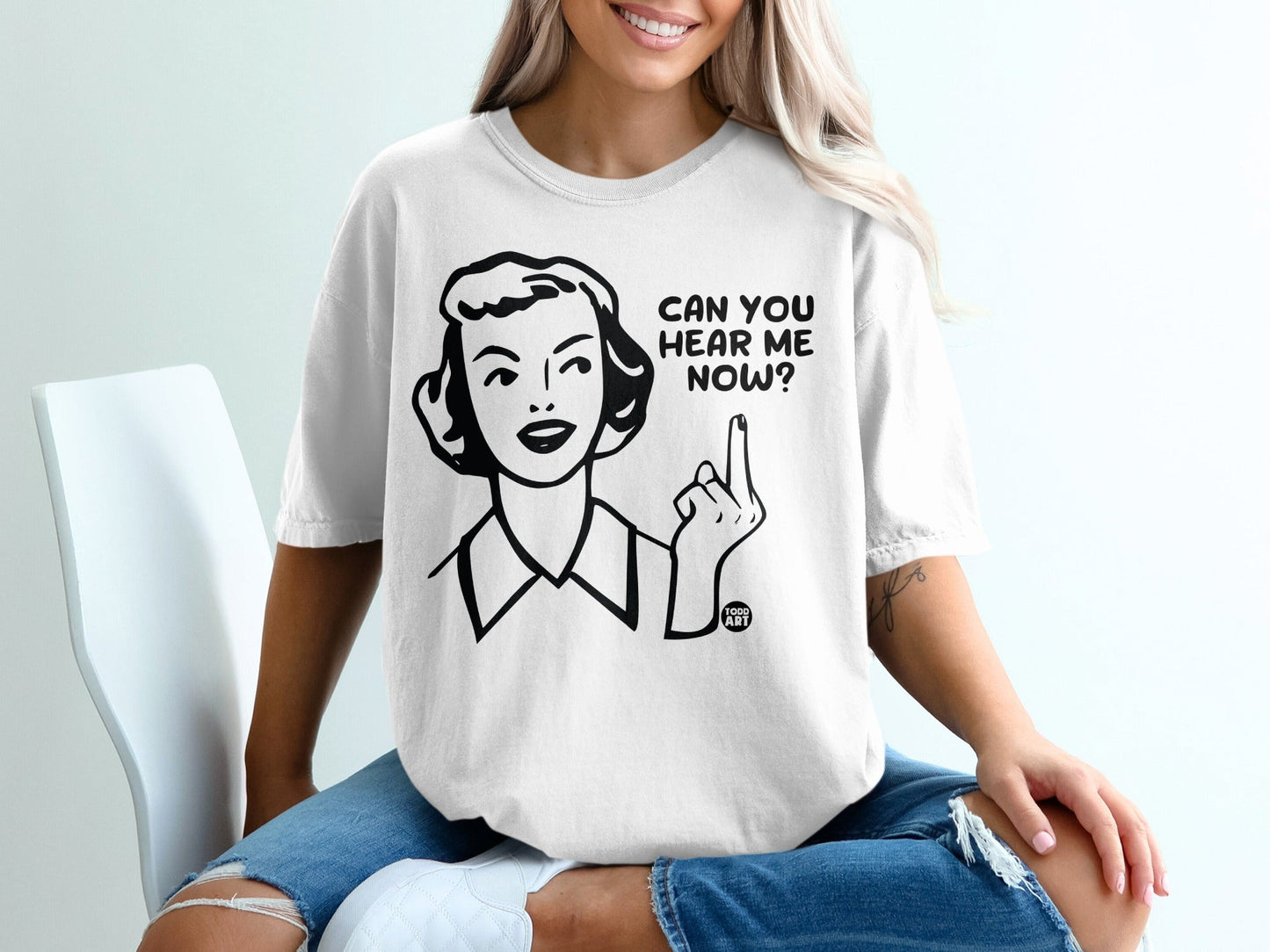 Woman wearing a white t-shirt with "CAN YOU HEAR ME NOW?" text and a middle finger graphic.
