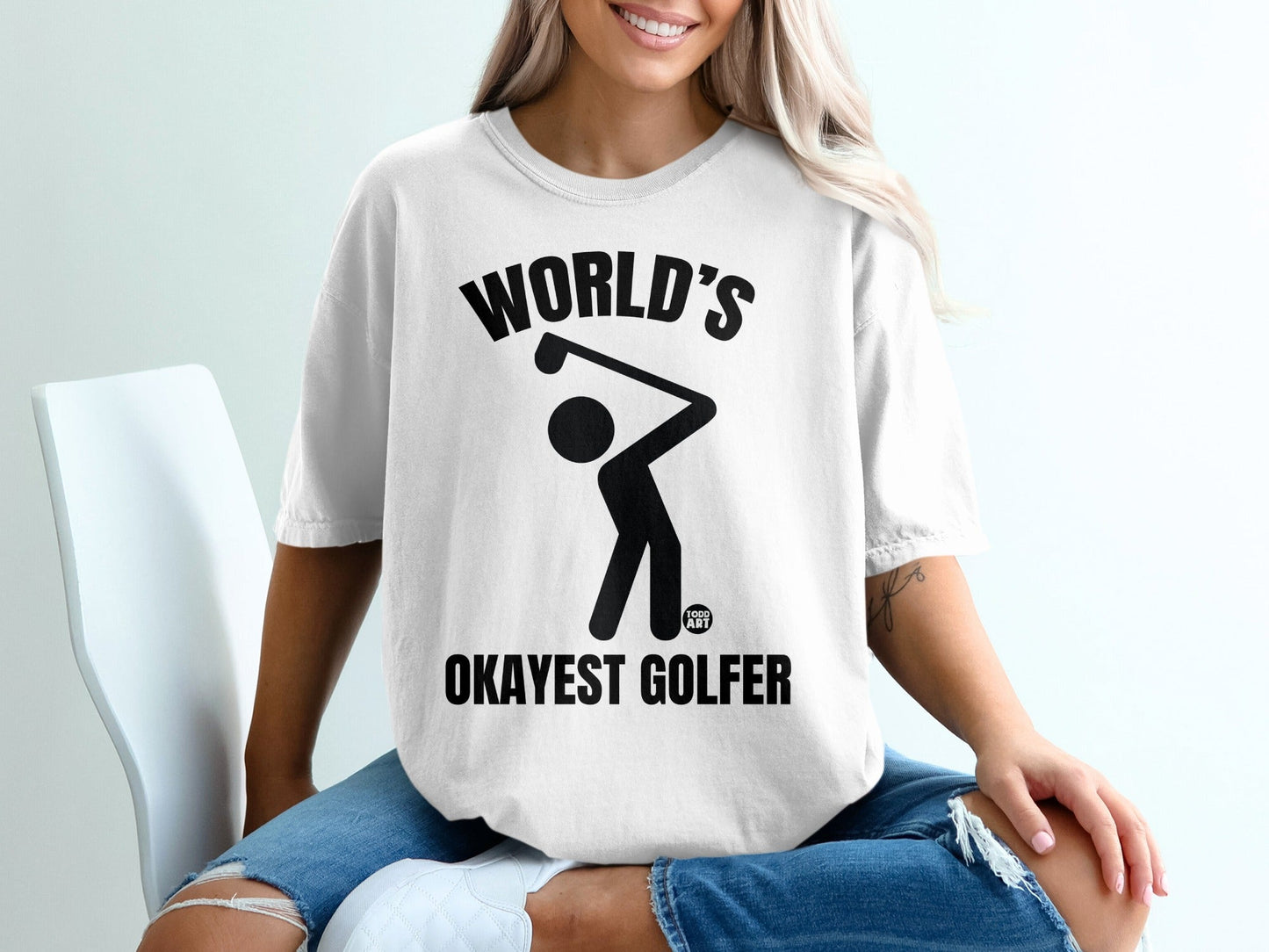 White t-shirt with "WORLD'S OKAYEST GOLFER" text and a golf swing graphic.