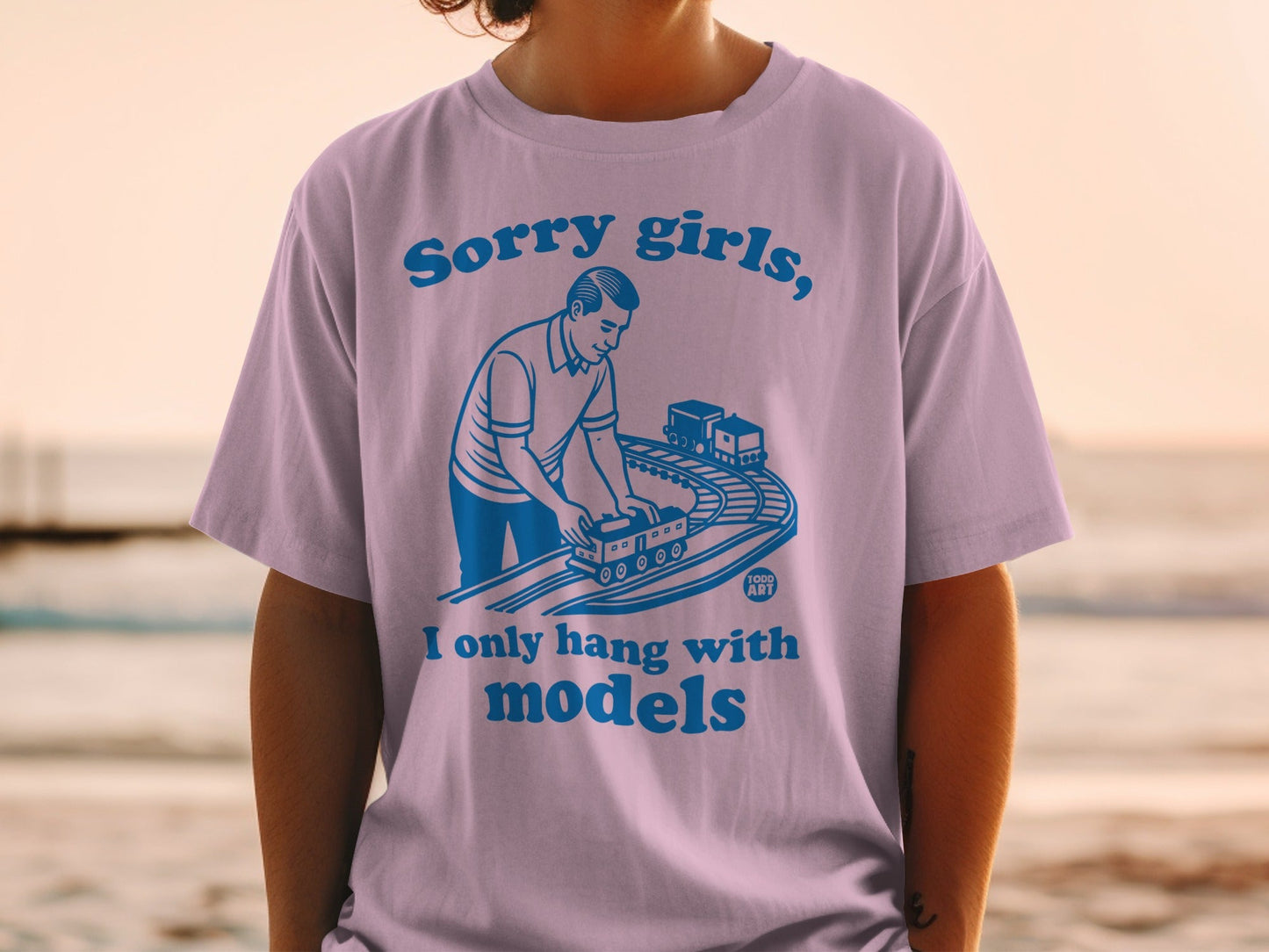 Purple t-shirt with blue text and illustration of man with model train set.