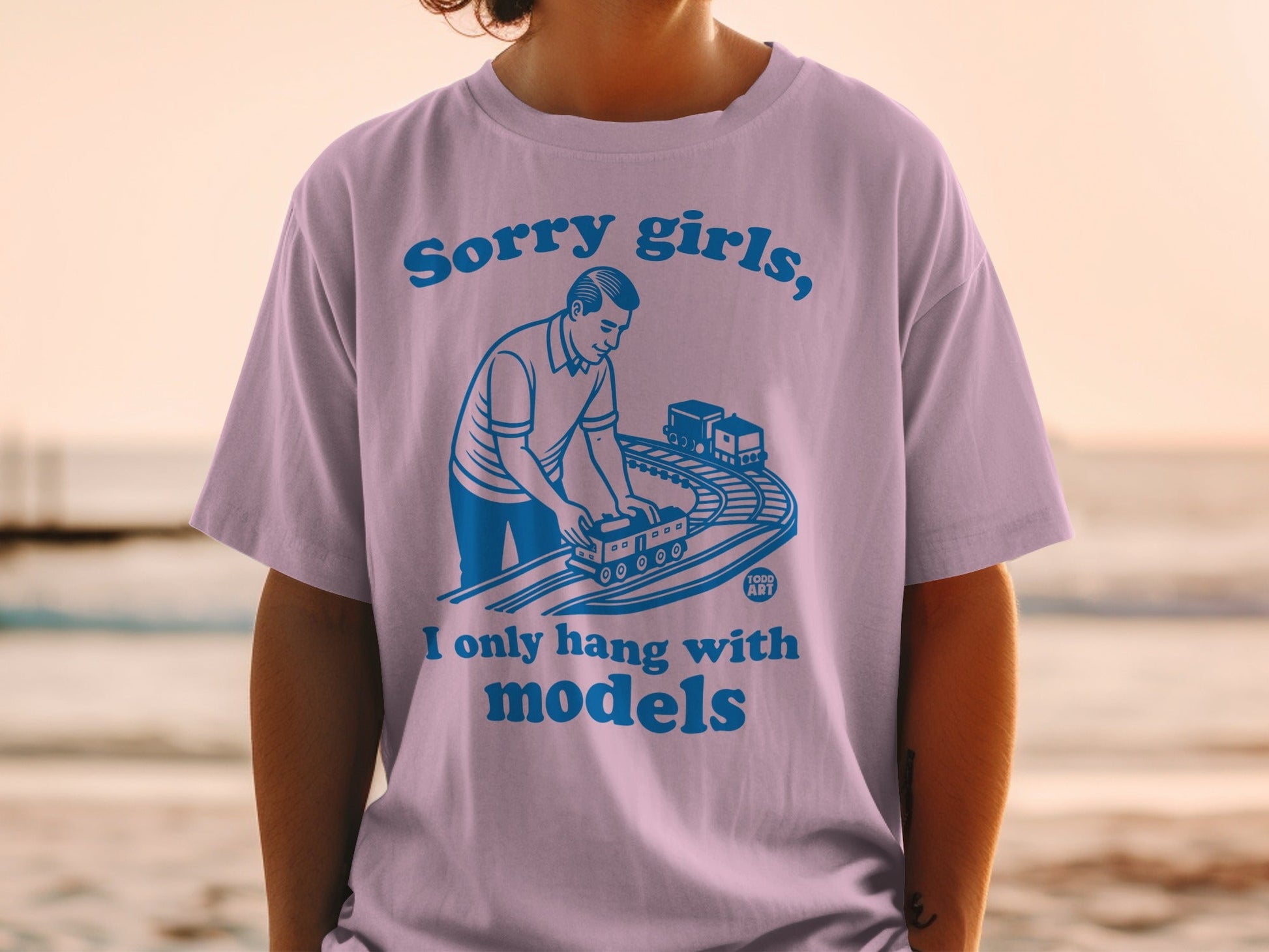 Purple t-shirt with blue text and illustration of man with model train set.