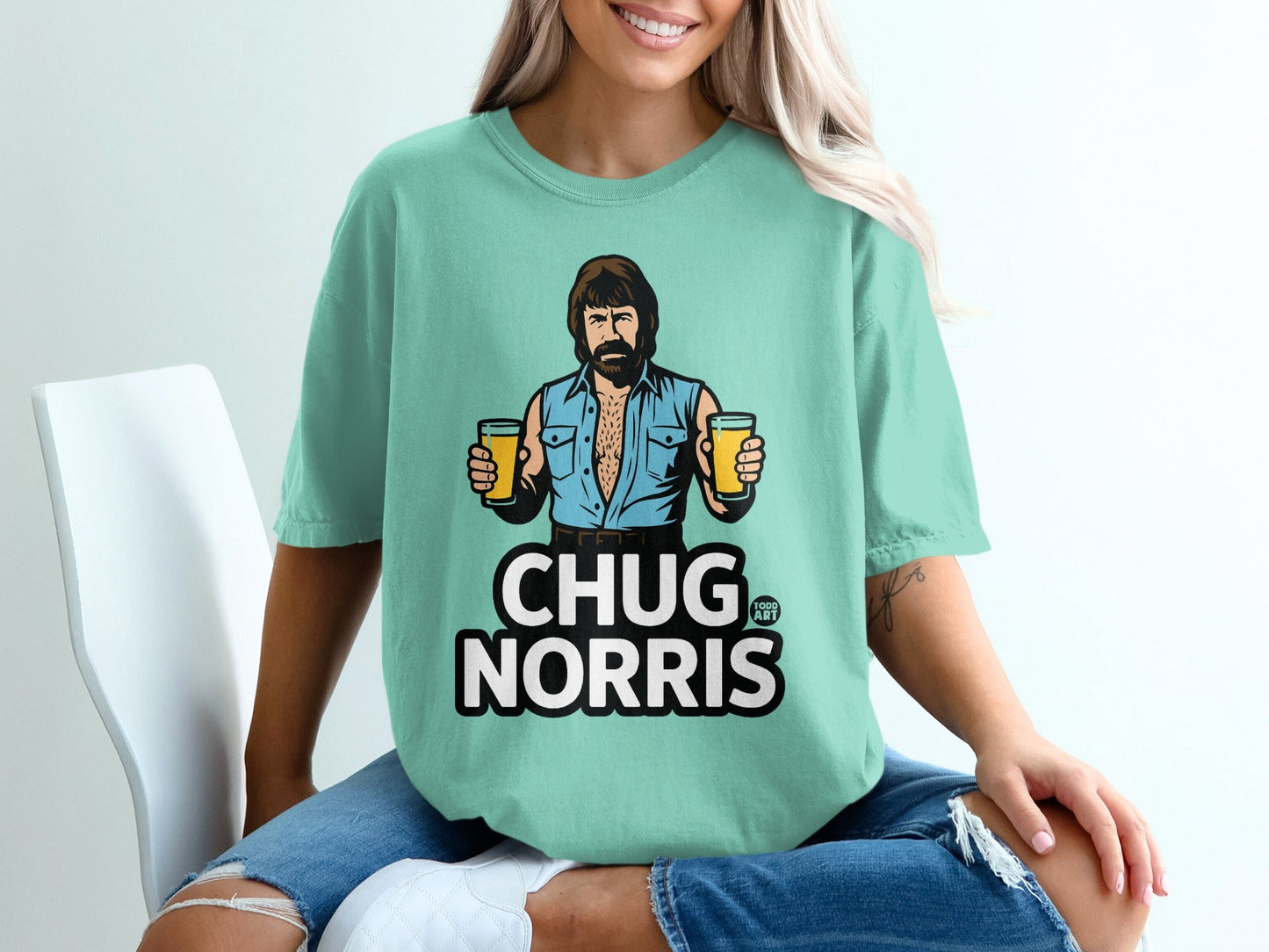 Woman wearing a teal t-shirt with Chuck Norris holding two beers.