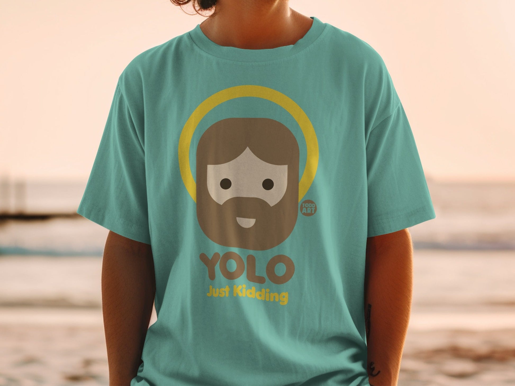 Teal t-shirt with cartoon Jesus saying "YOLO Just Kidding" and halo.