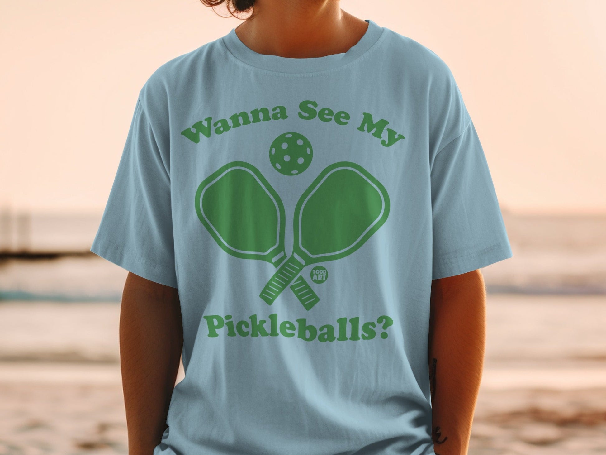 Light blue t-shirt with green text and pickleball graphic.