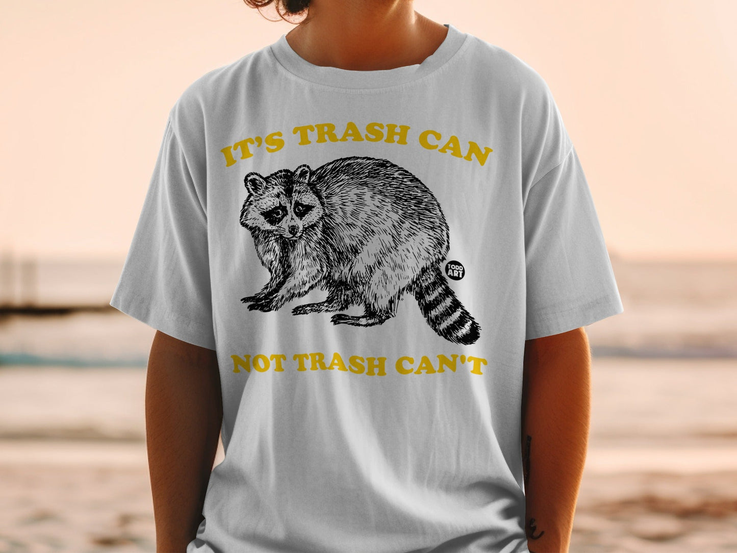 T-shirt with a raccoon graphic and text "IT'S TRASH CAN NOT TRASH CAN'T".