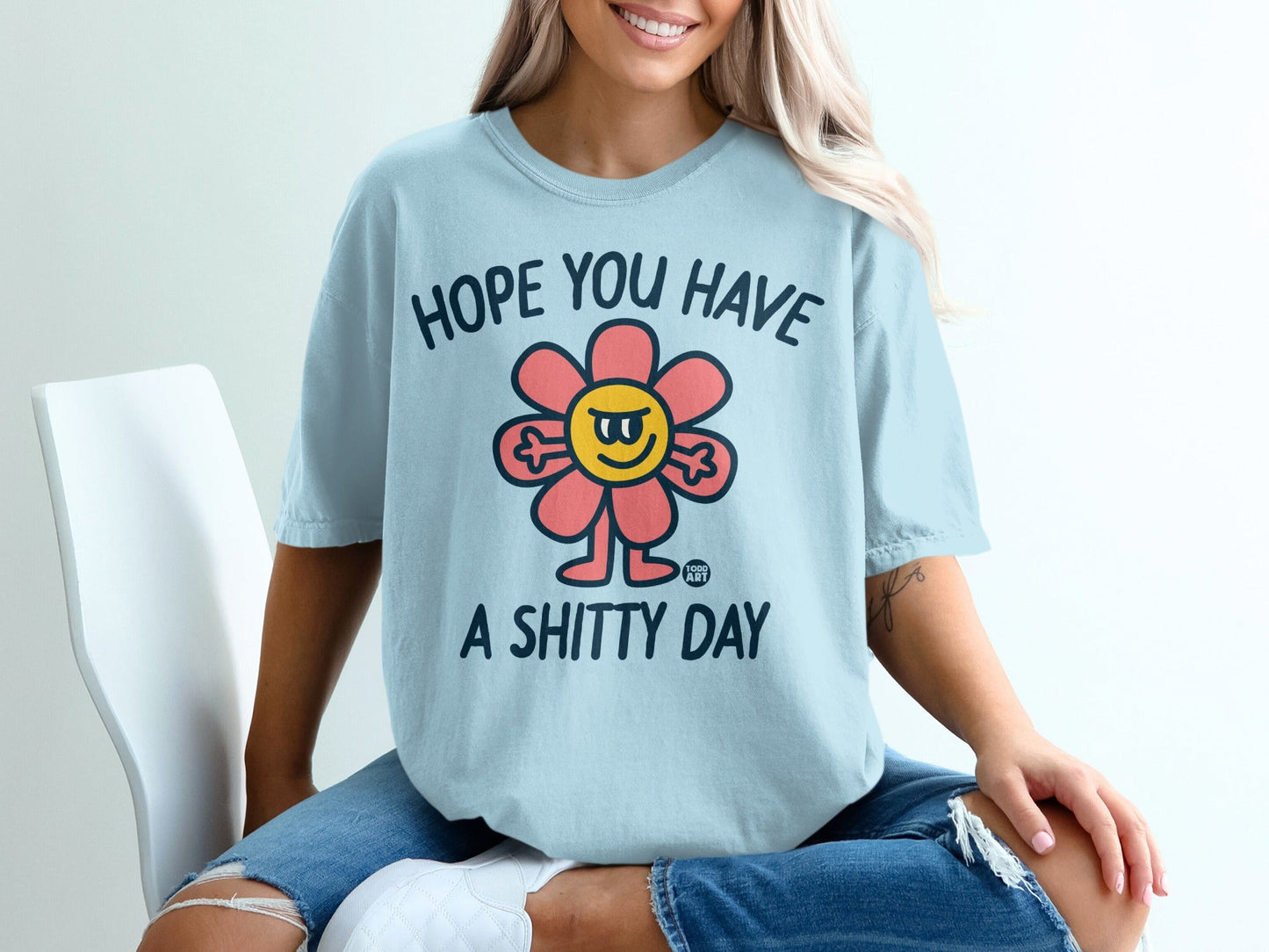 Light blue t-shirt with a cartoon flower saying "HOPE YOU HAVE A SHITTY DAY".